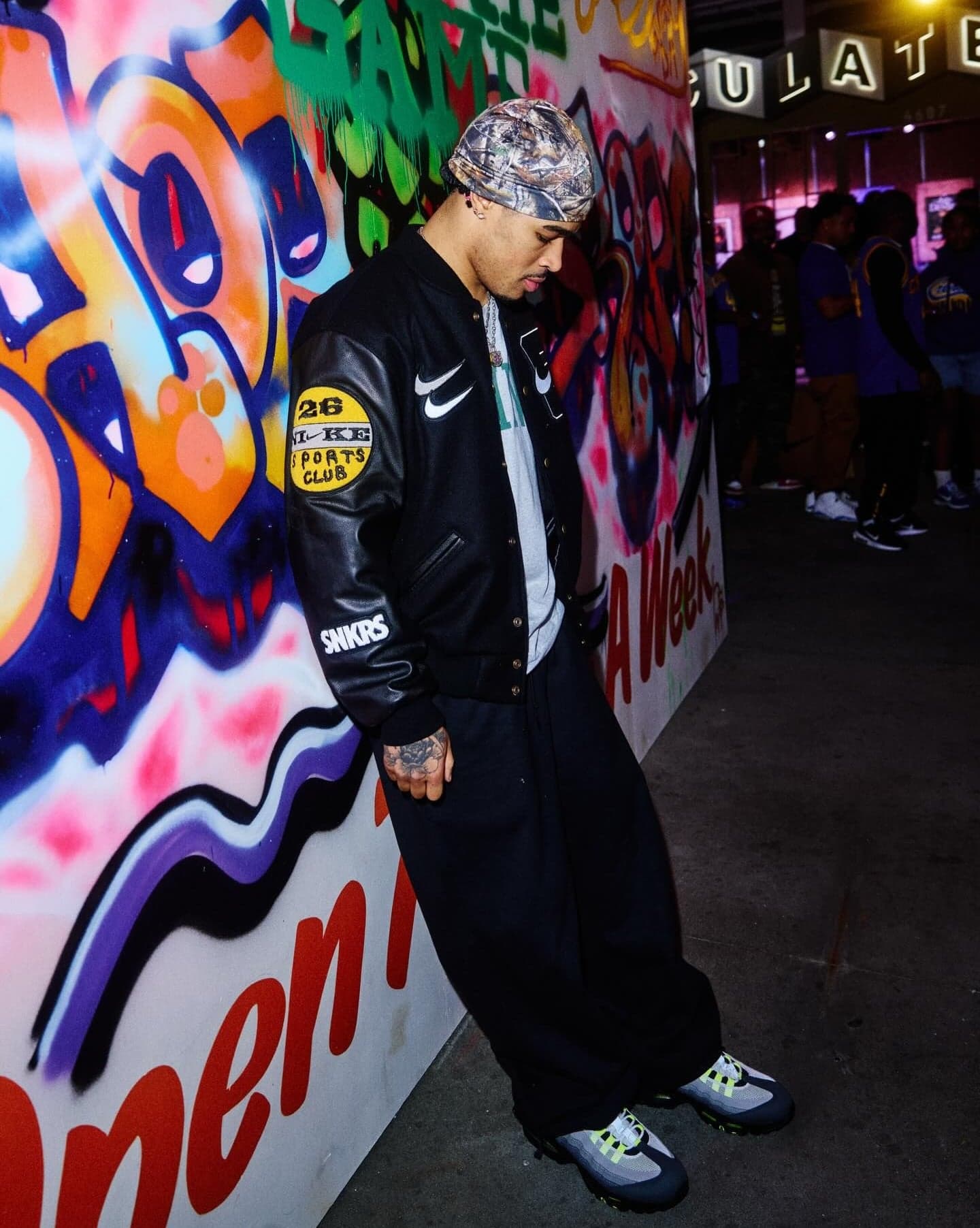 A guest in a varsity jacket leaning against a graffiti mural