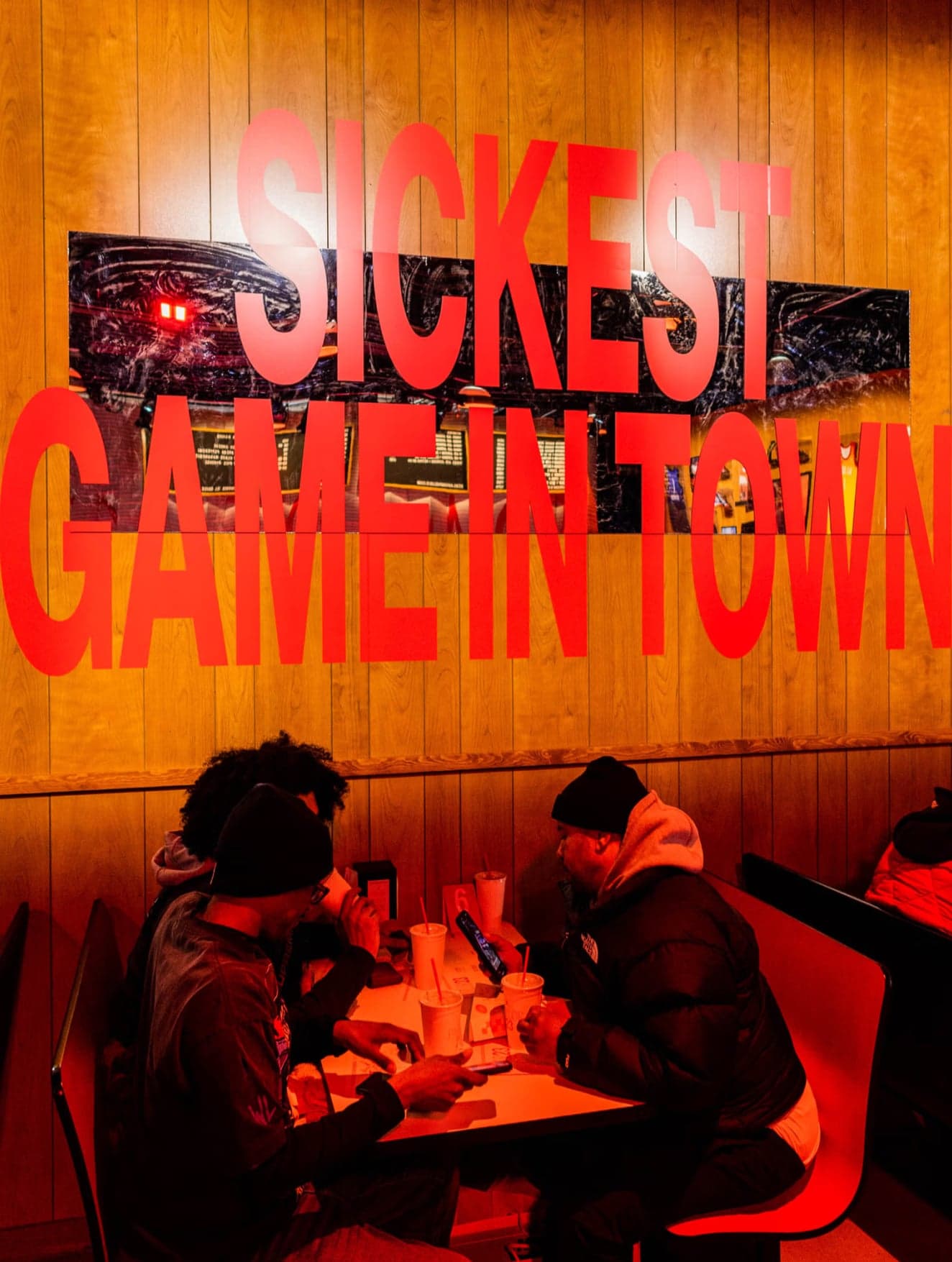 Guests eating in a wood-panelled booth under red “Sickest game in town” lettering