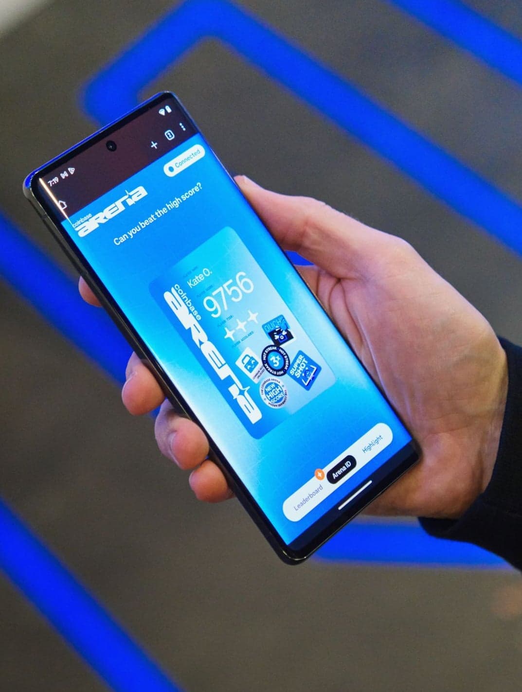 A hand holding a phone showing the Coinbase Arena microsite