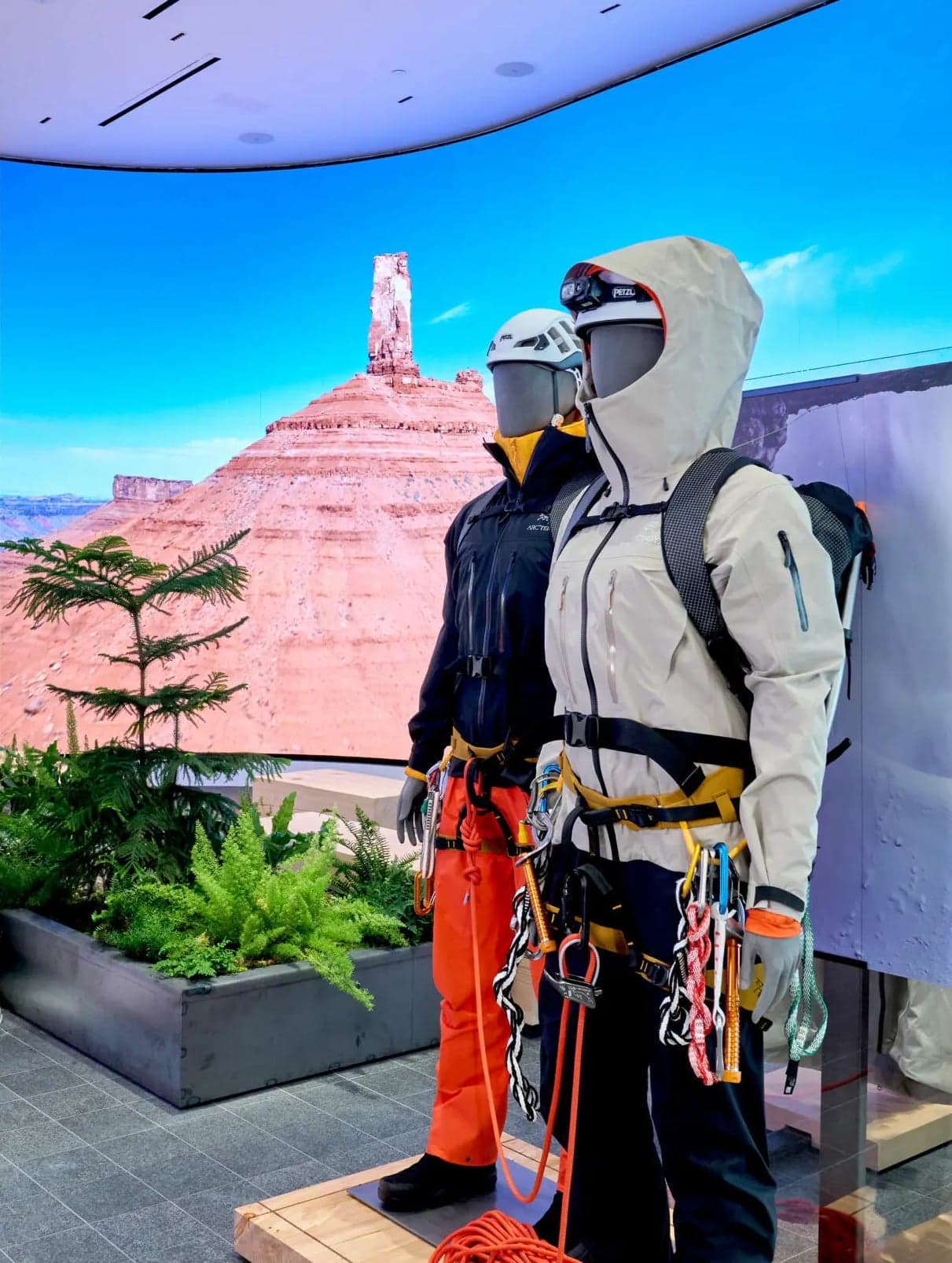 Mannequins in climbing gear in front of a curved LED wall showing desert cliffs