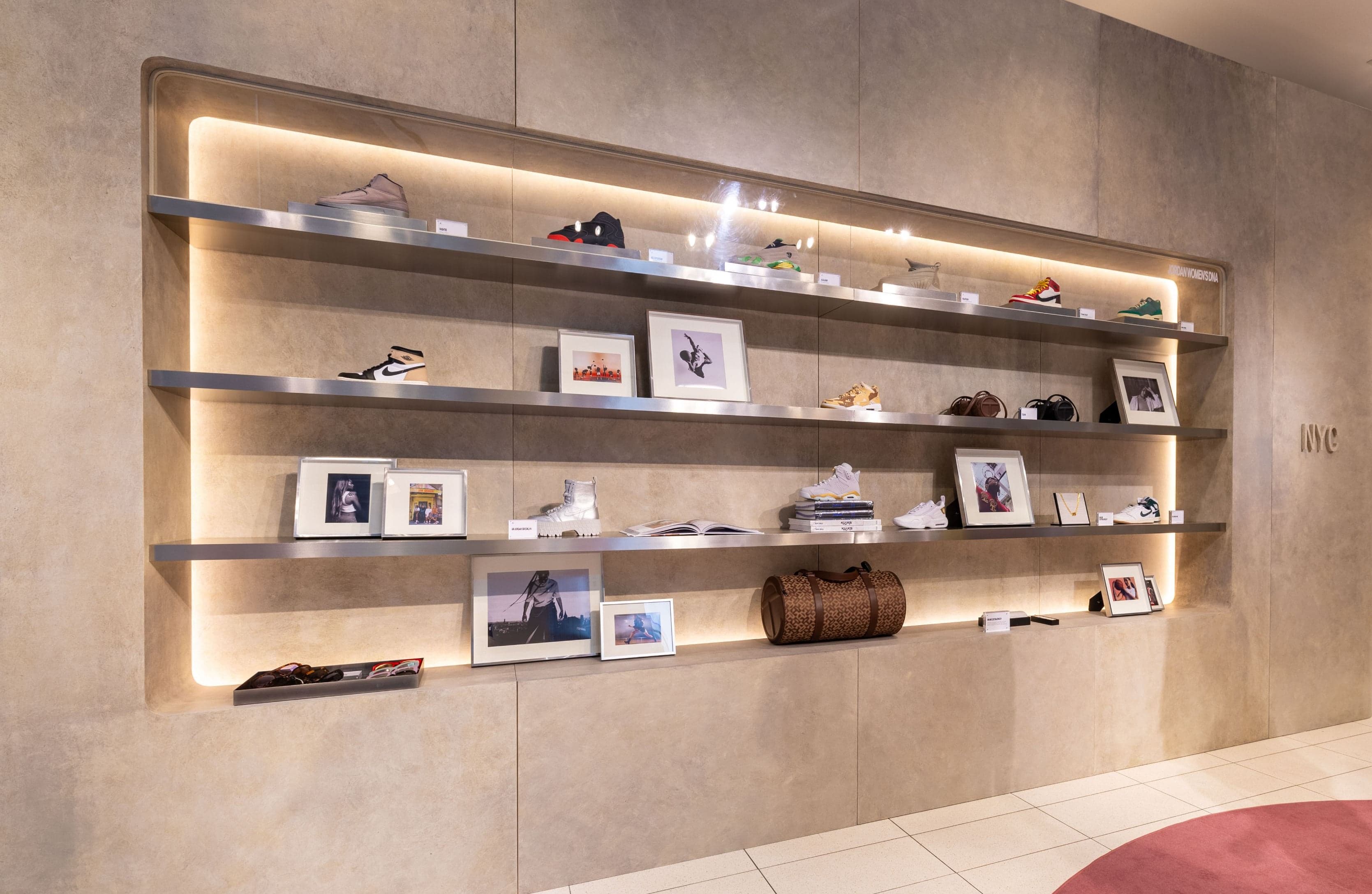 A lit, recessed shelf wall of sneakers, bags and framed photos