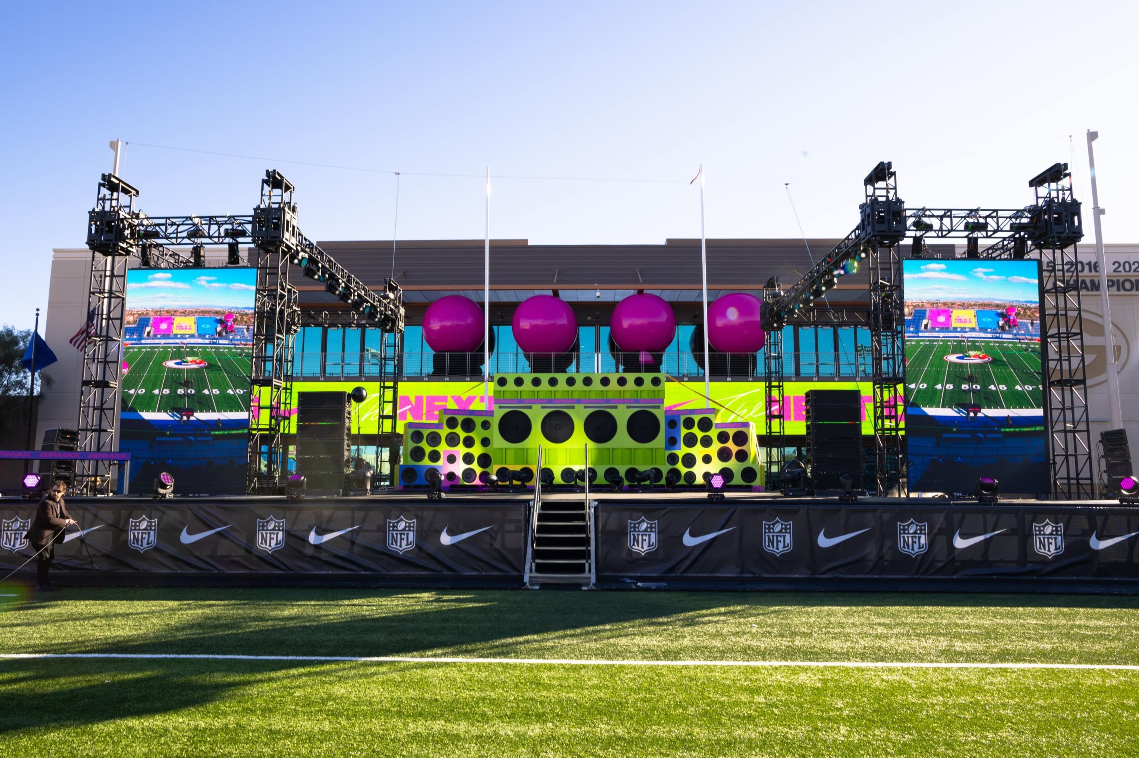 The event stage between two LED screens, with pink spheres and a neon green speaker wall