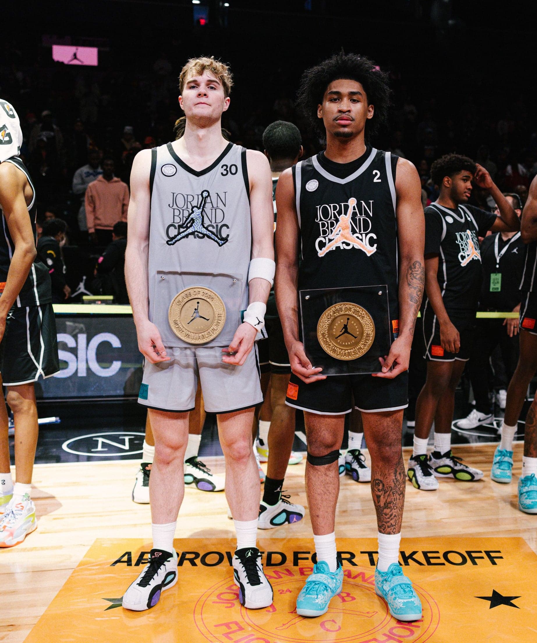 Two players holding gold medallions on court, teammates behind them