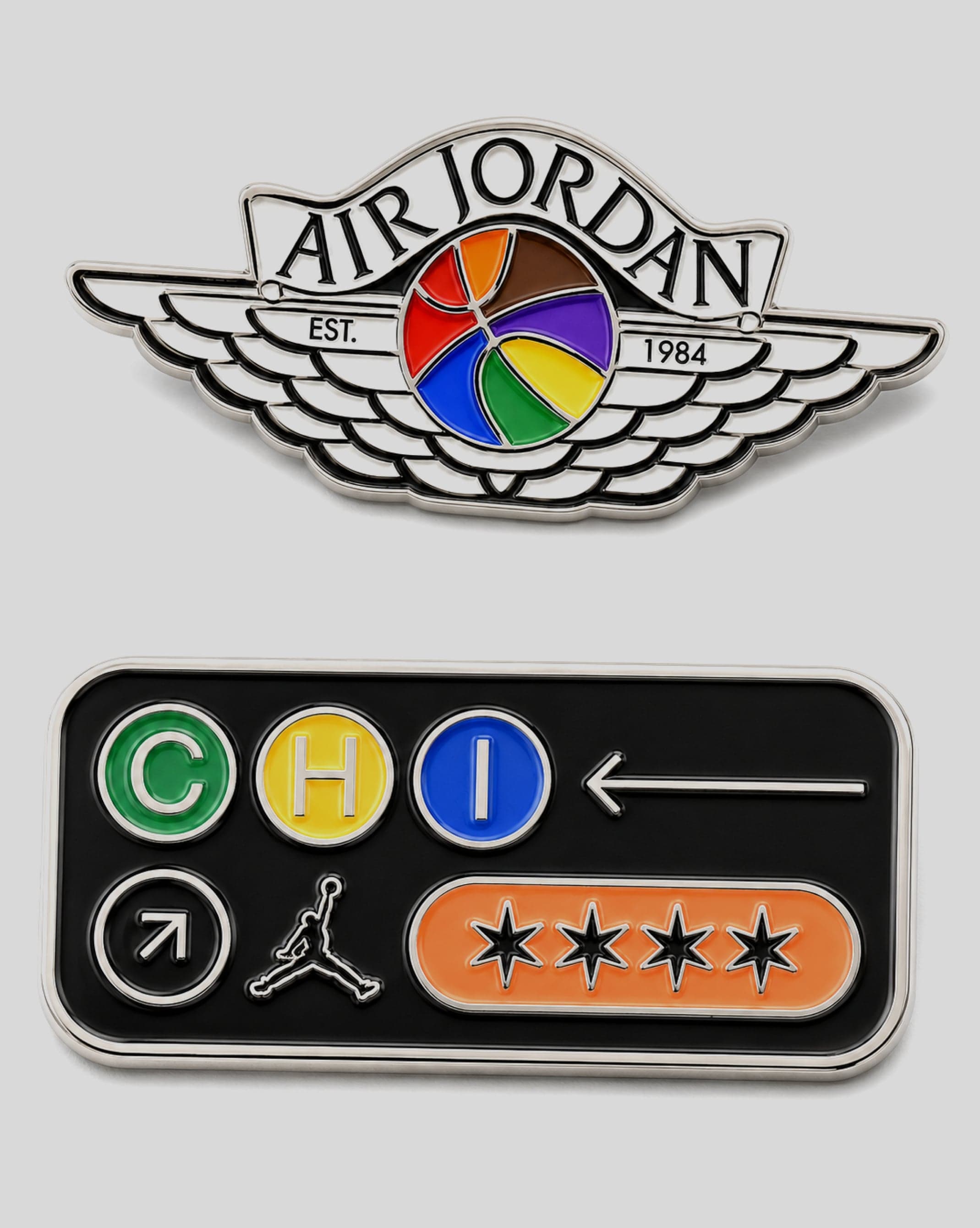 An Air Jordan wings pin with a rainbow basketball, and a Chicago CHI pin with the Jumpman and four red stars, on a grey card