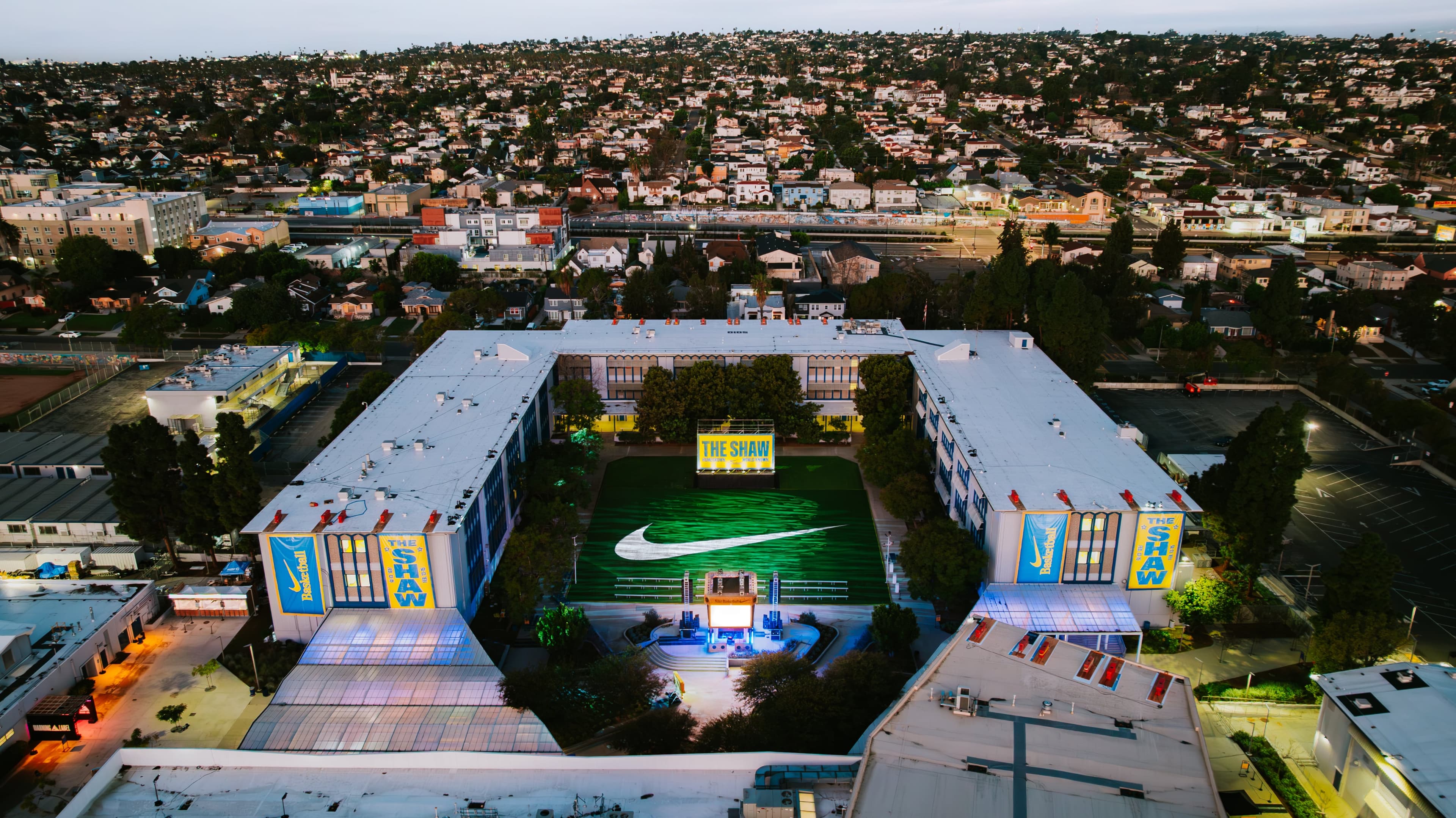 Aerial view of Crenshaw High School at dusk, its courtyard court lit up with a Nike swoosh