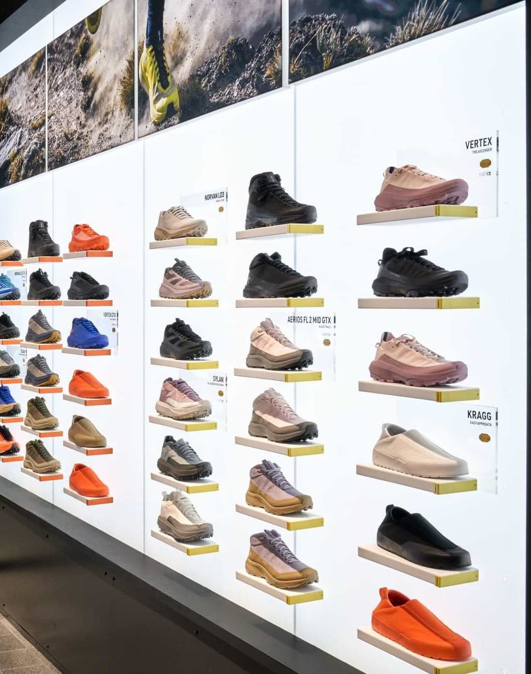 A lit wall of hiking shoes and backpacks under mountain photography