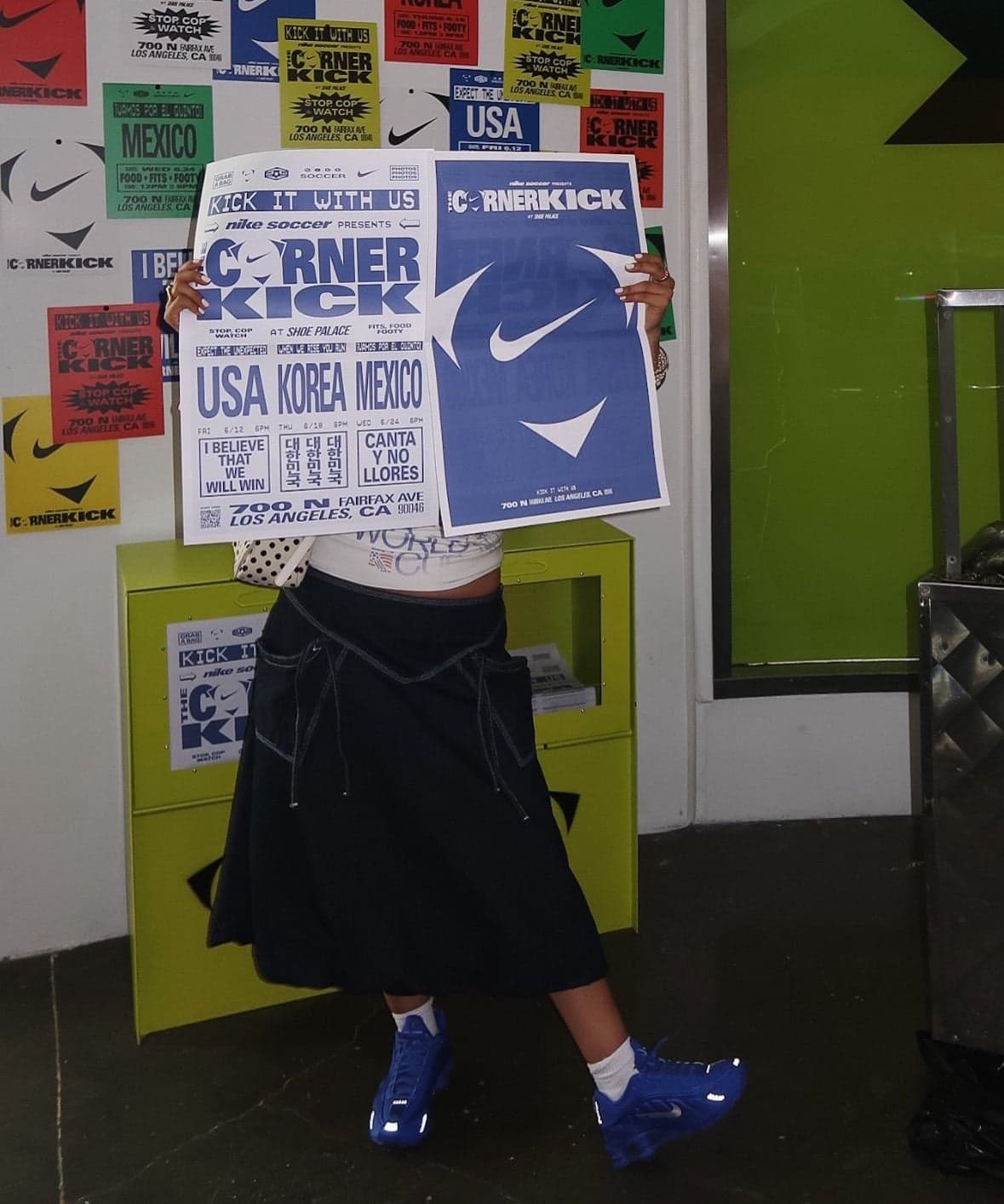 A guest holding up Corner Kick posters in front of a wall of stickers