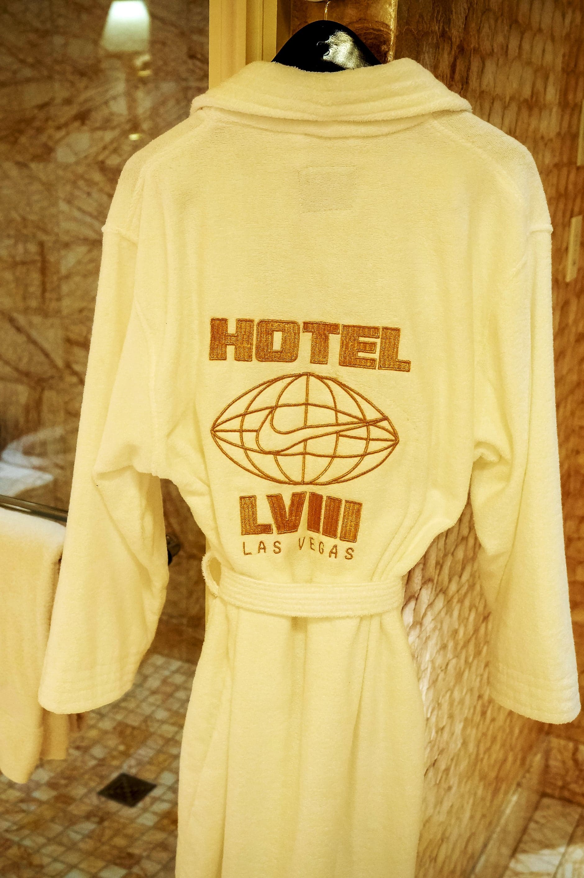 A cream Hotel LVIII Las Vegas bathrobe hanging in a marble bathroom