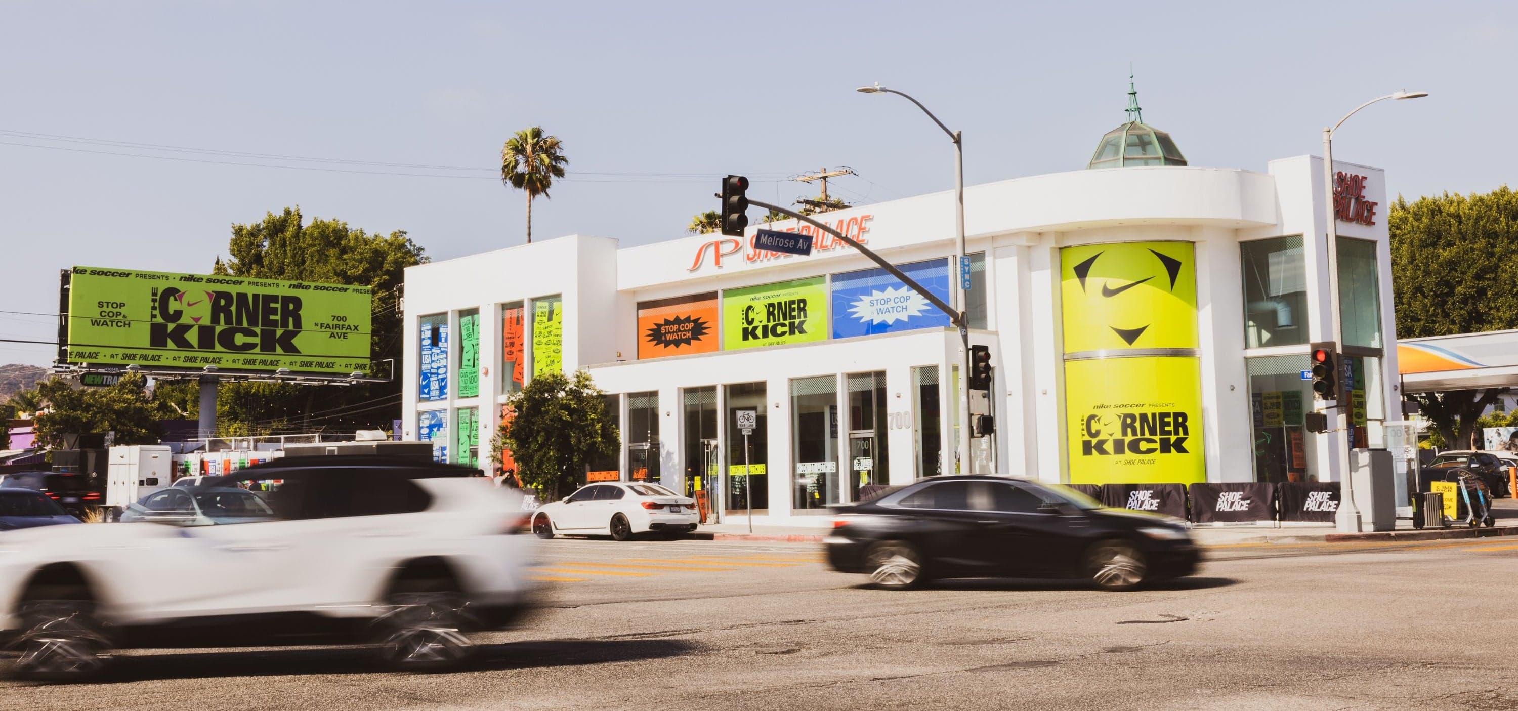 The Shoe Palace building on Melrose and Fairfax, wrapped in Corner Kick graphics, with traffic passing
