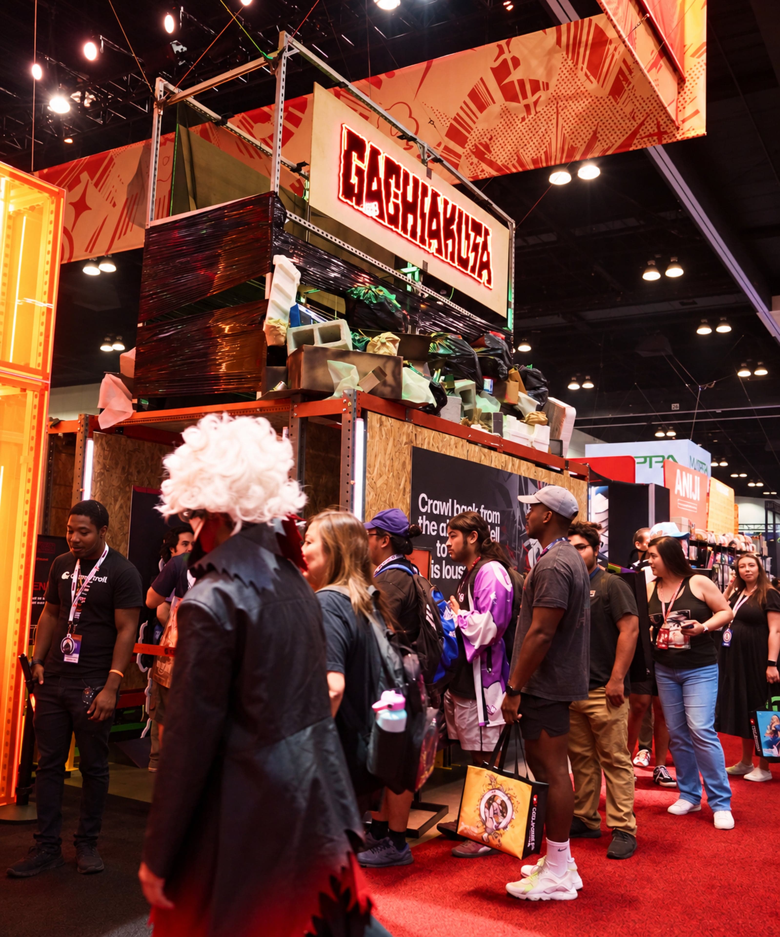 Fans, one in white-haired cosplay, queueing under the Gachiakuta sign and a tower of trash props