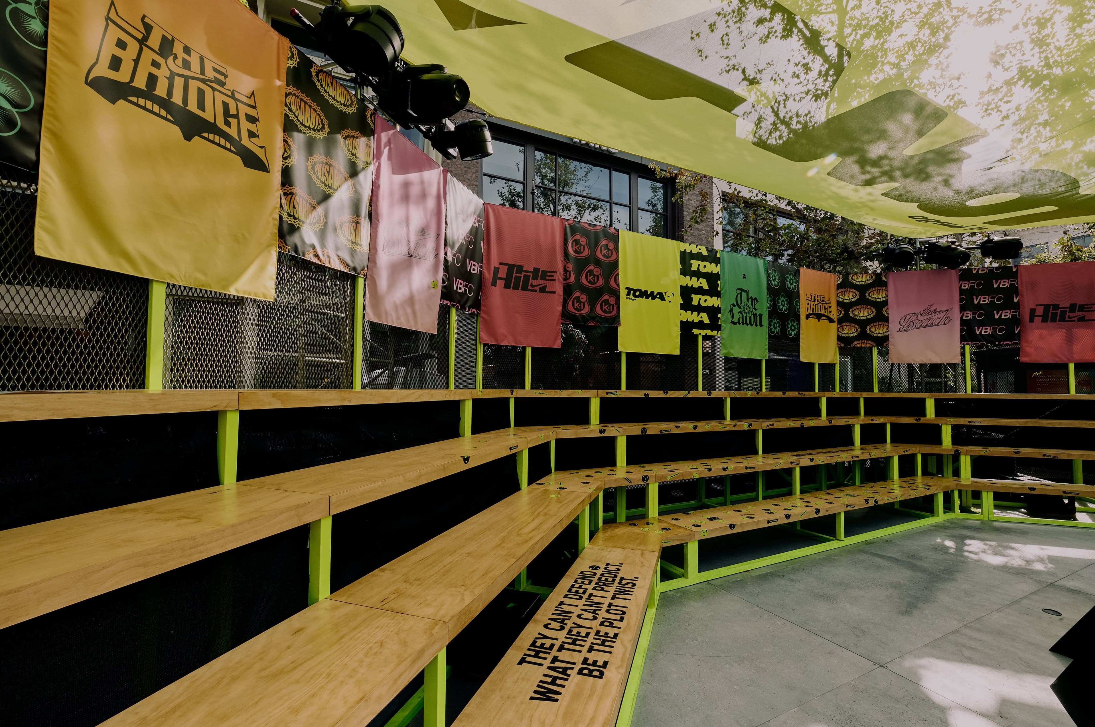 Bleachers under hanging banners and towels along the pitch