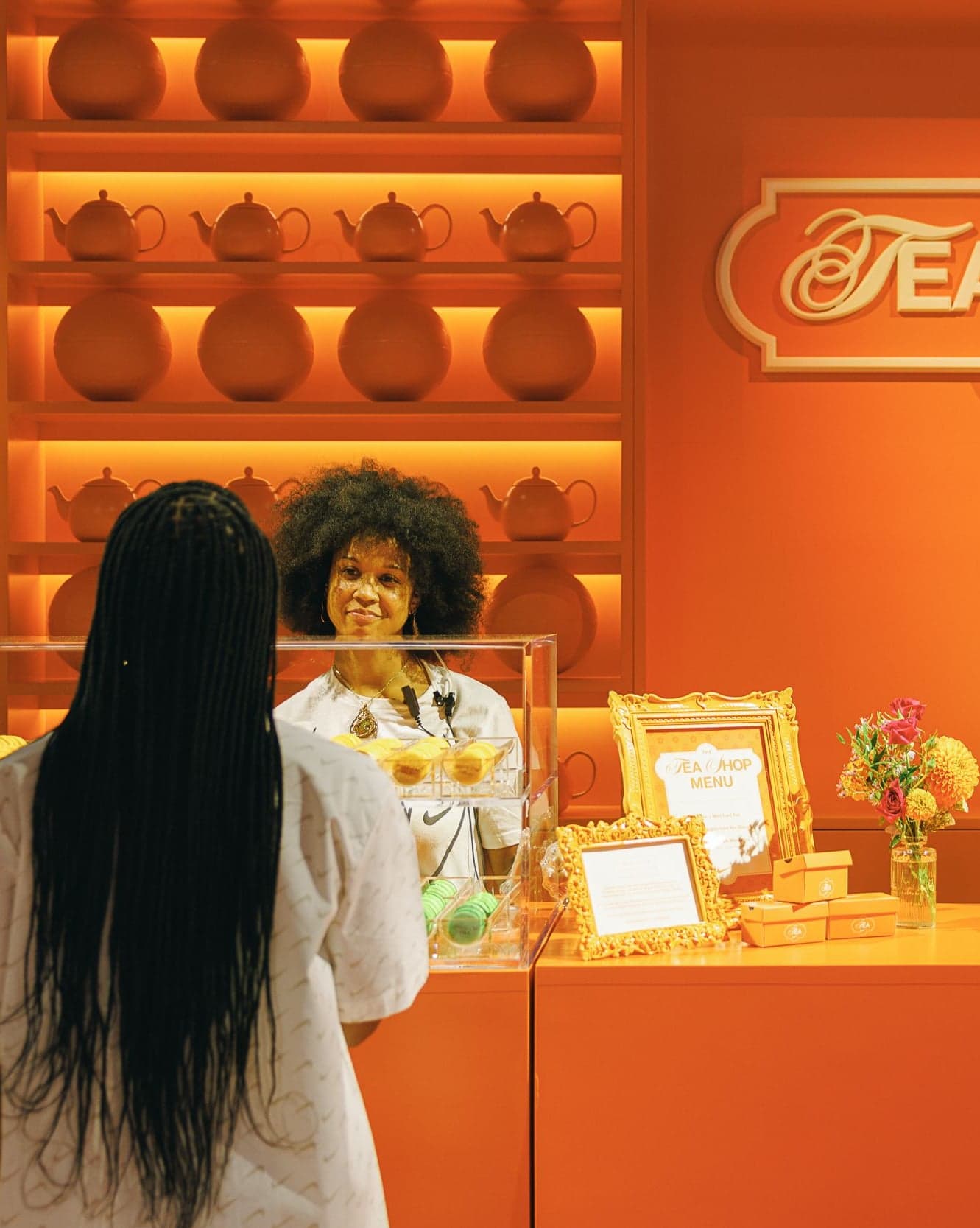 A guest at the Tea Shop counter under shelves of orange teapots
