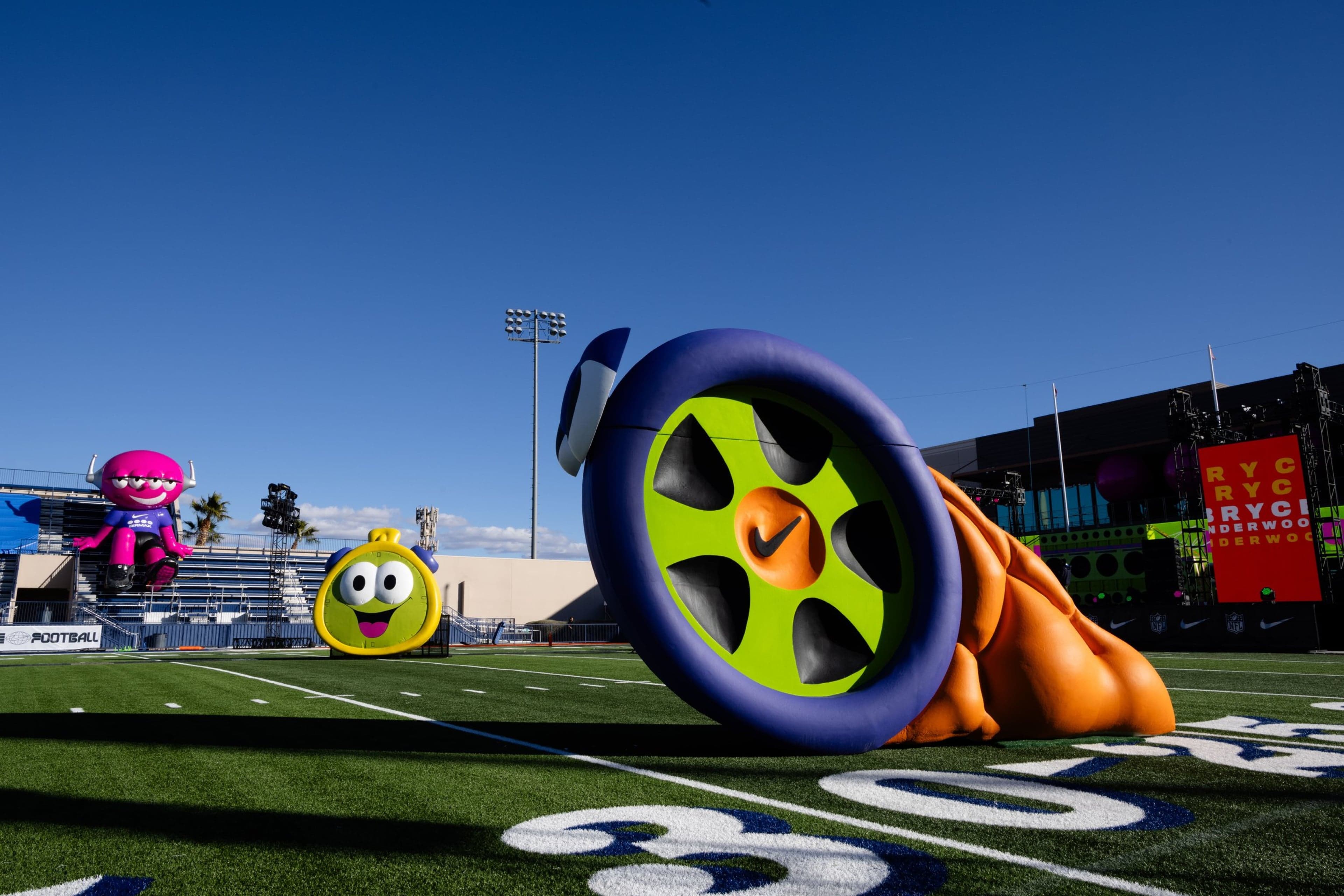 A giant inflatable wheel and orange slide on the field, with inflatable characters in the end zone