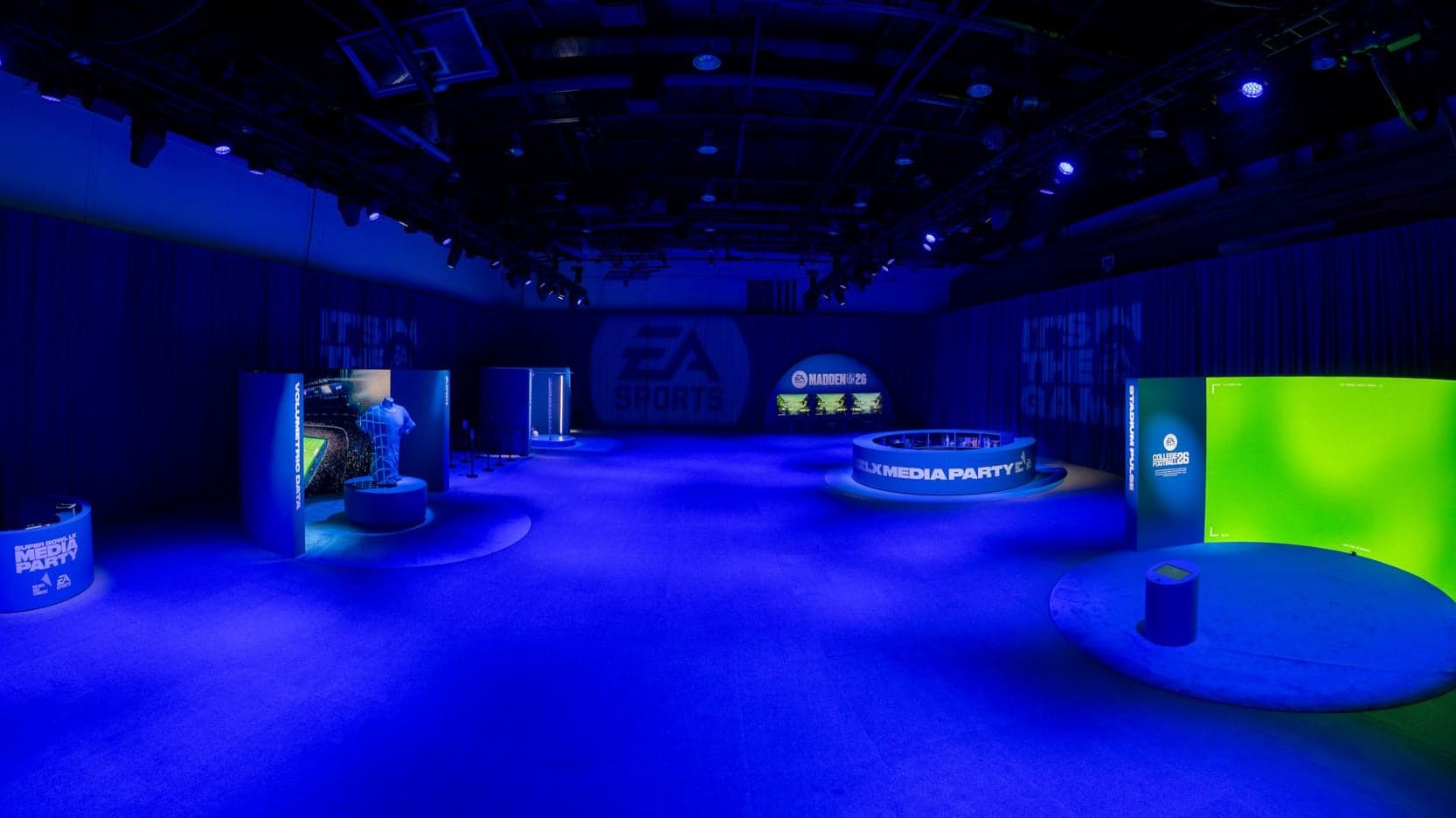 The Innovation Station event floor lit in blue, with game booths around the room and a green screen stage on the right