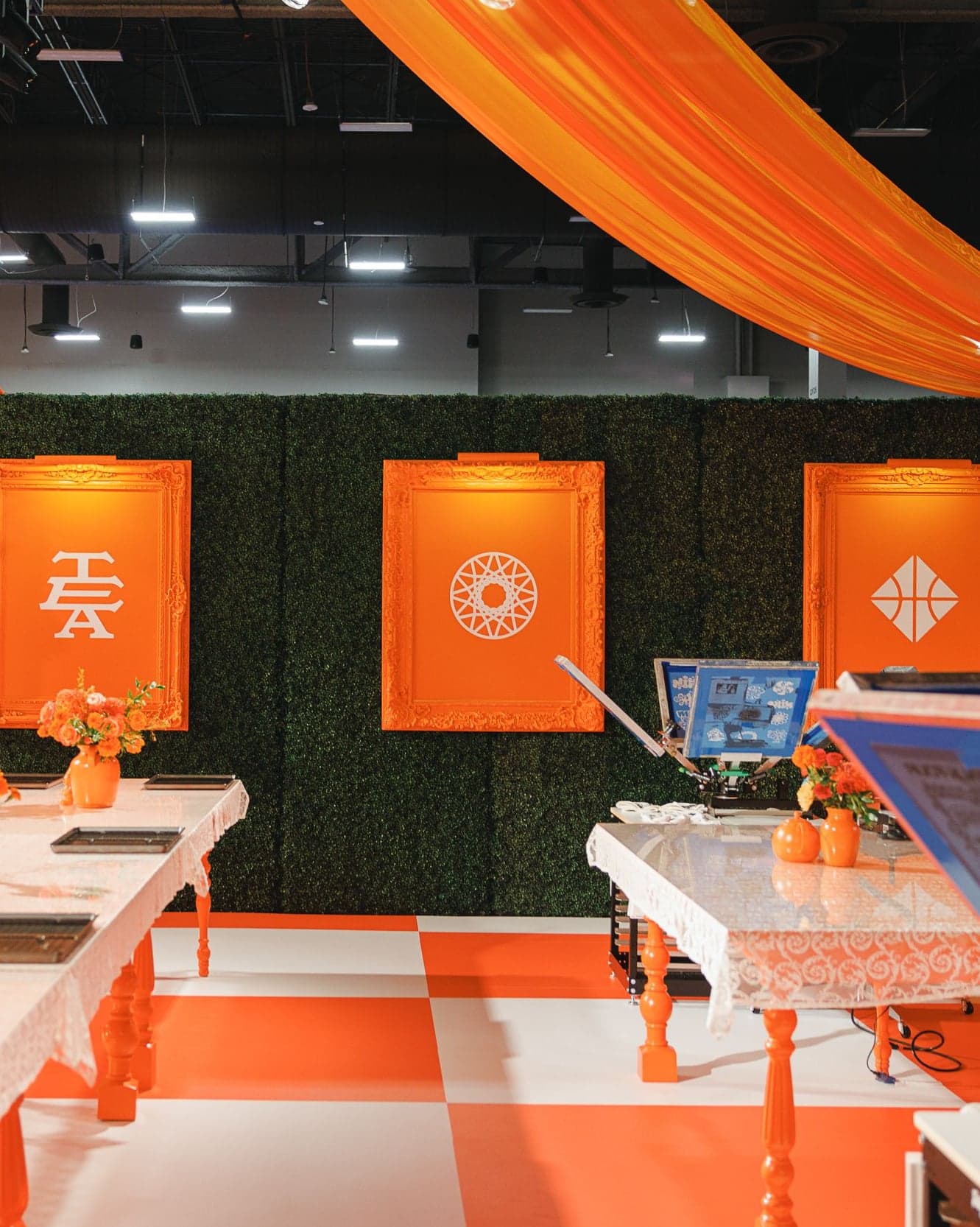 Printing tables in front of hedge walls hung with orange panels