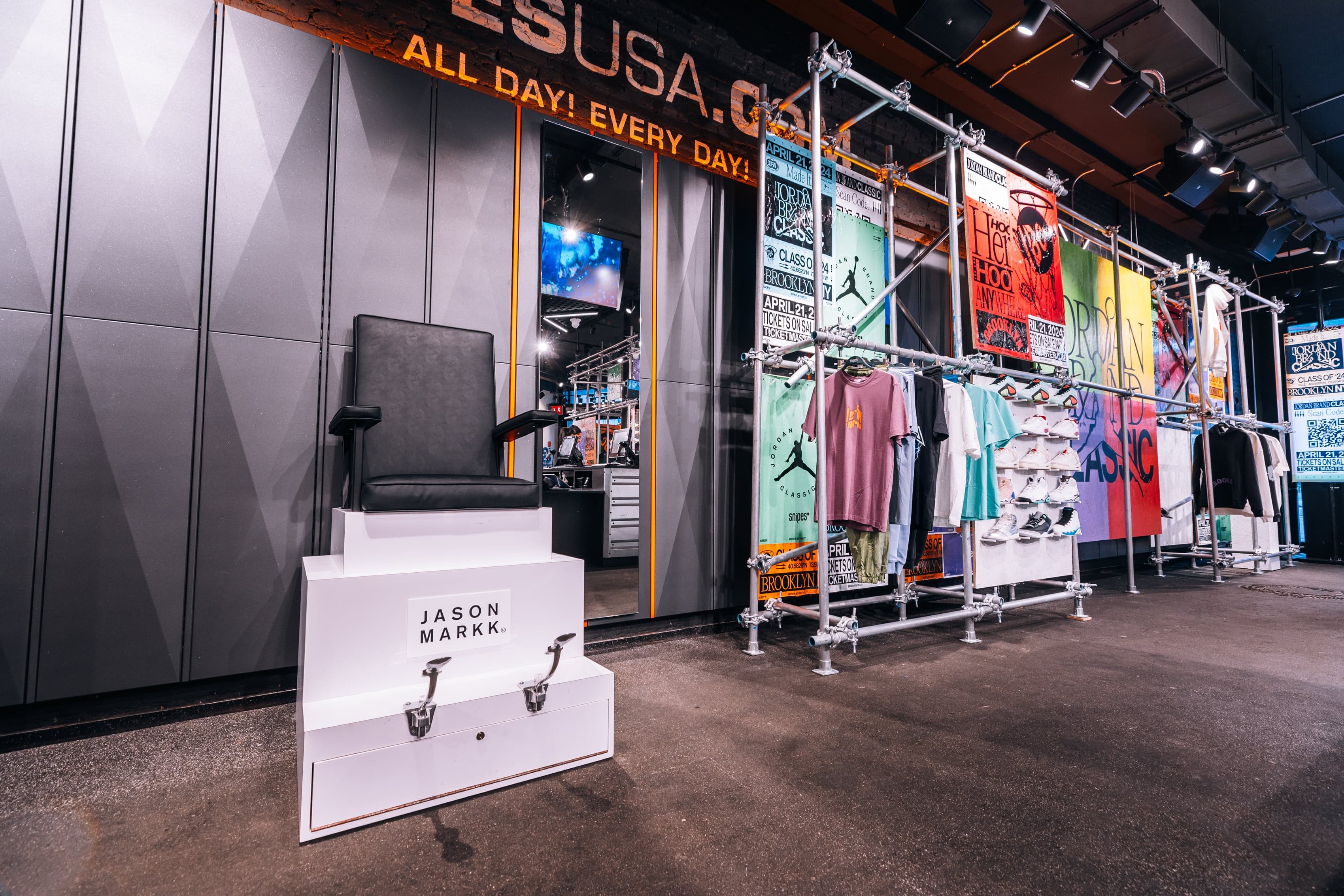 A shoe-shine chair on a white plinth beside racks of colorful apparel