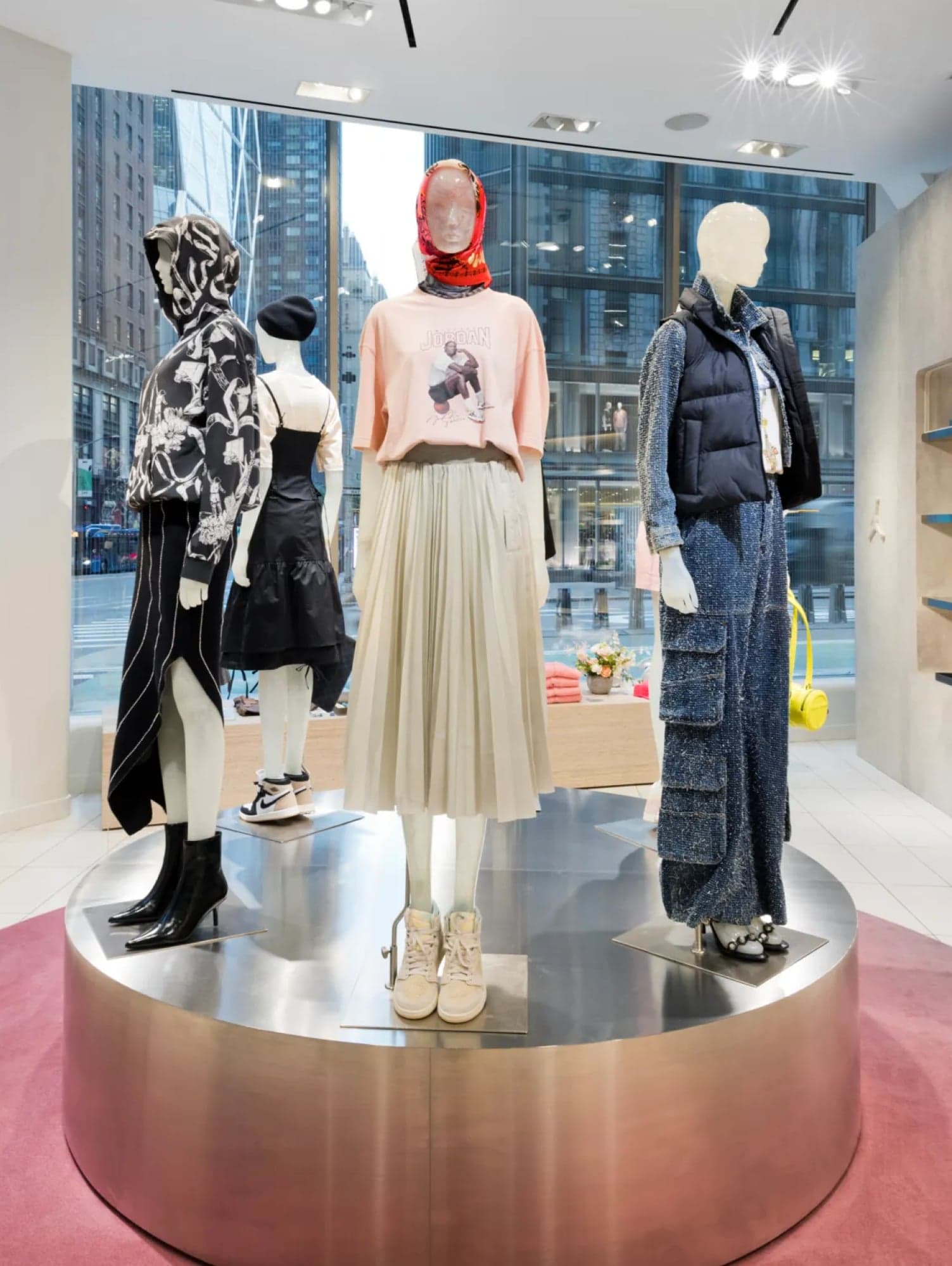 Three mannequins in streetwear on a round steel plinth by the window