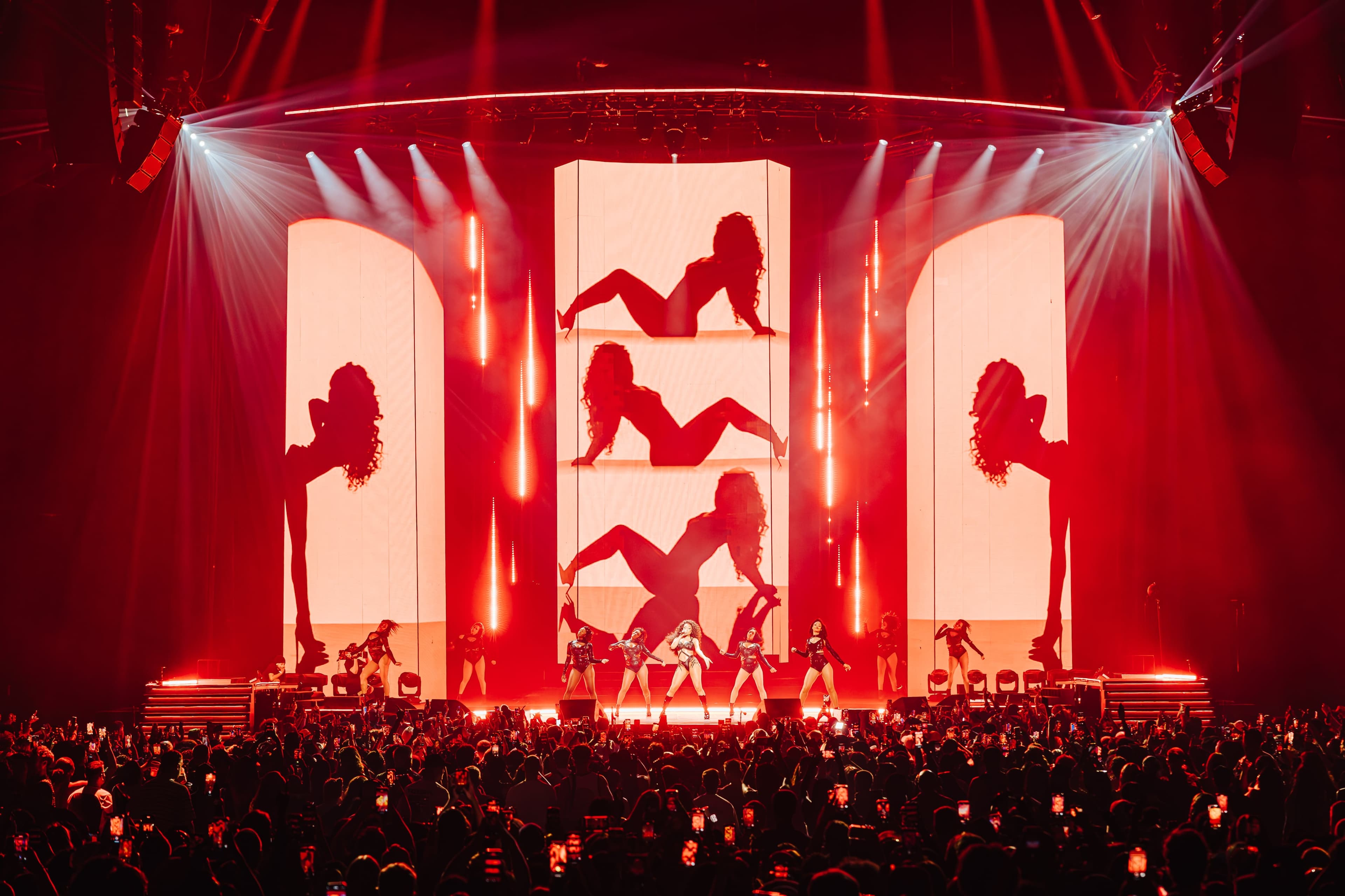 Dancer silhouettes on glowing red-and-cream screens above the stage