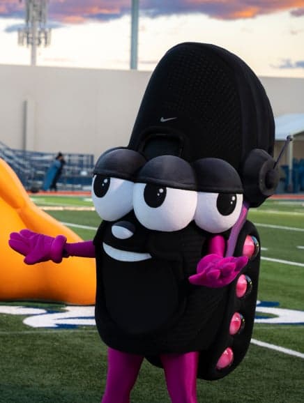 A black, big-eyed mascot with headphones and a Nike swoosh, waving on a football field