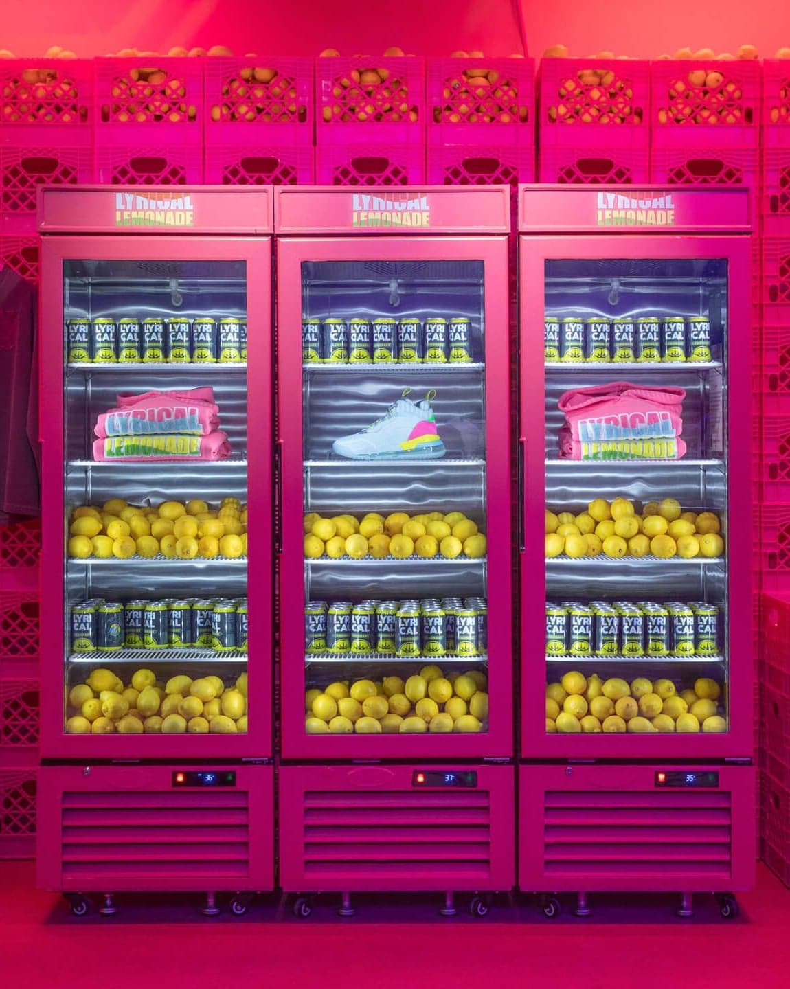 Pink fridges full of drinks and lemons in front of a wall of pink crates