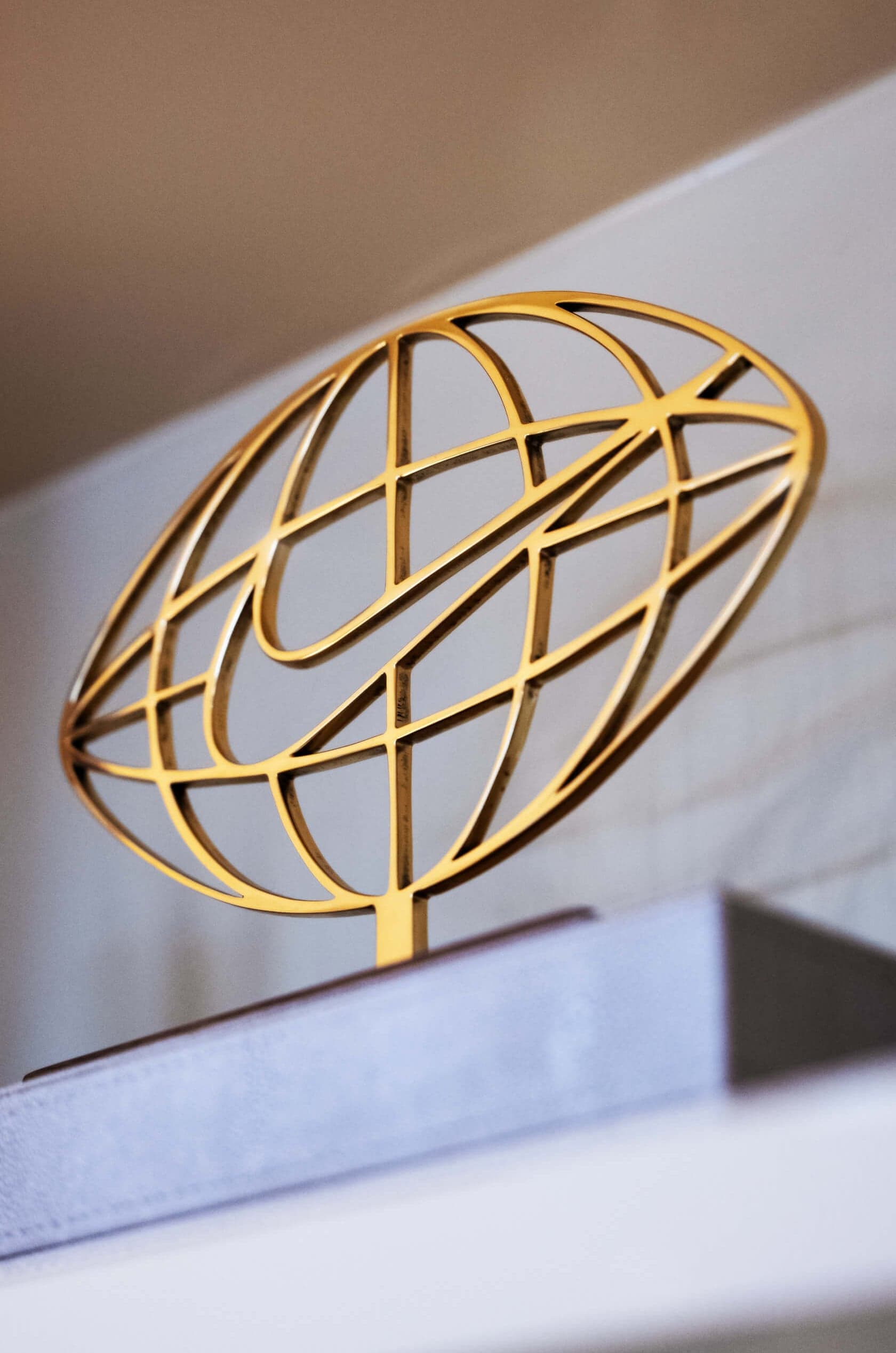 A gold globe-and-swoosh sculpture on a white shelf