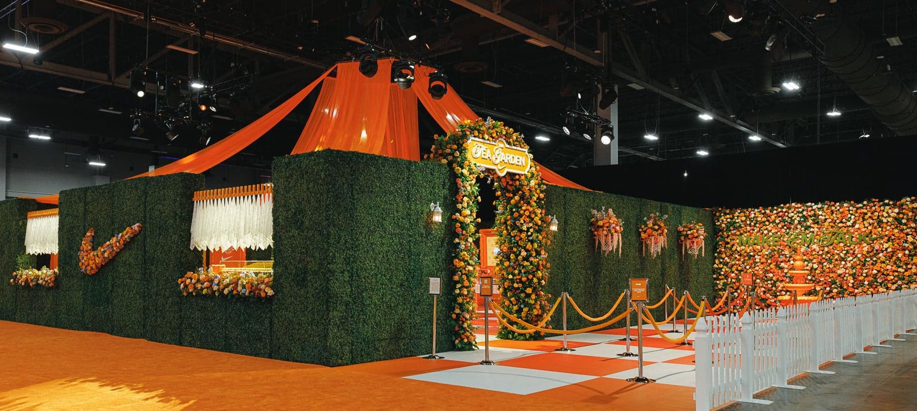 The Tea Garden booth: hedge walls and a floral arch under orange drapes on an orange floor