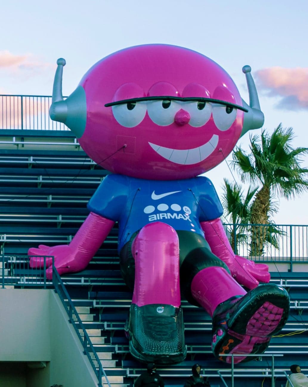 A pink inflatable alien mascot sitting in the stands above the helmet tunnel and a crowd on the sideline