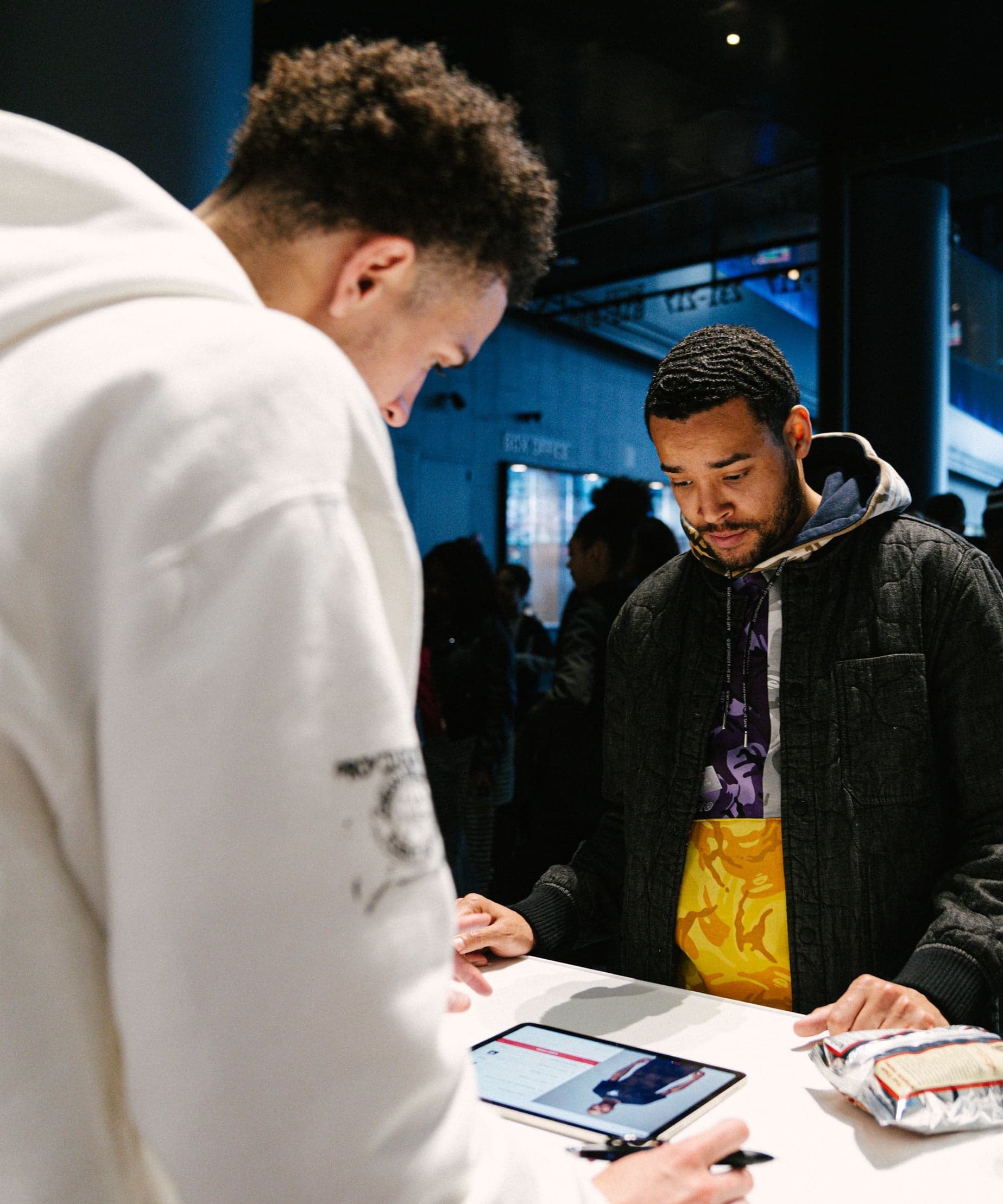 Guests at a counter, one in a white hoodie checking a tablet