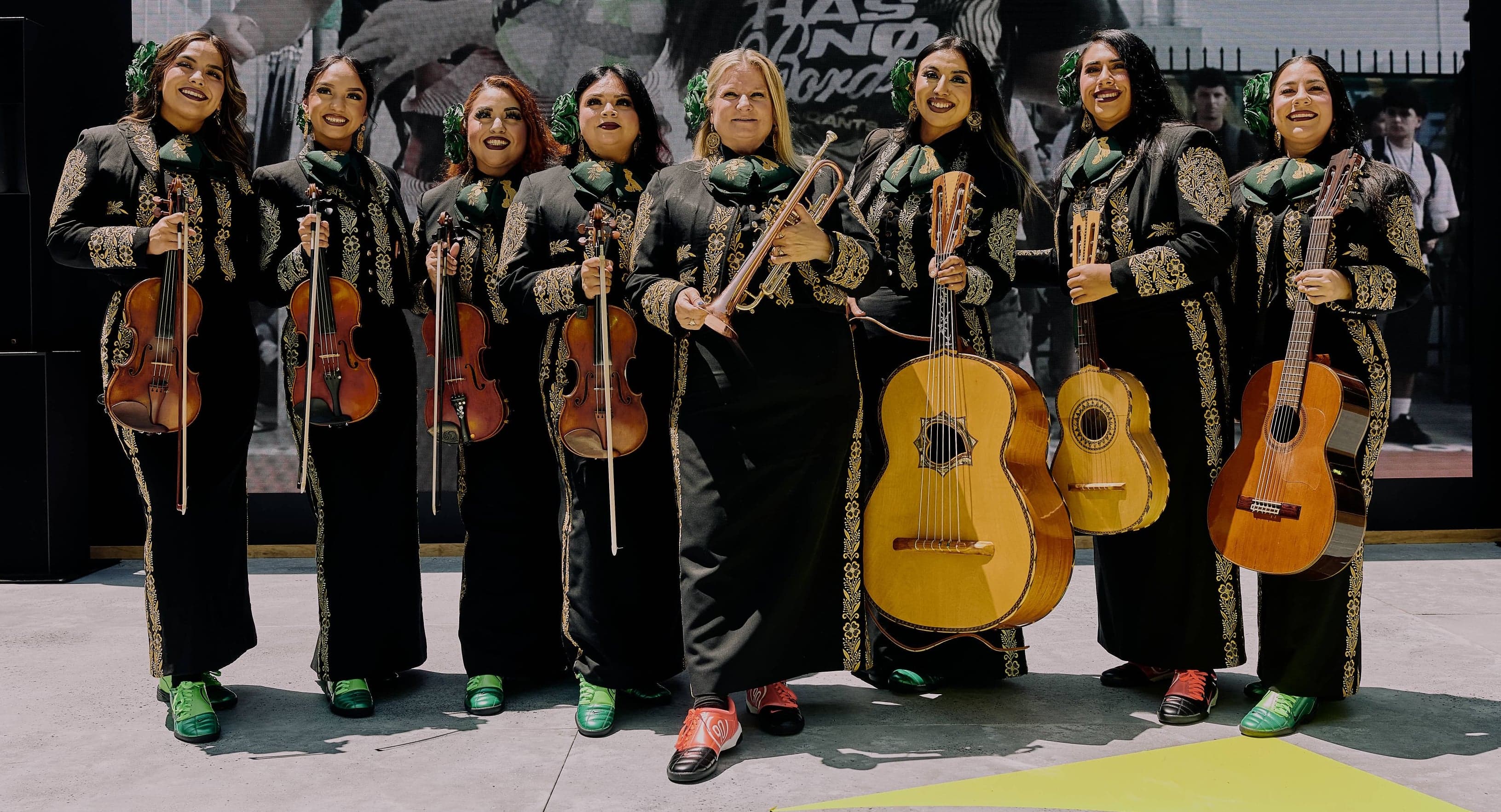 A mariachi band of women in black charro suits posing with their instruments