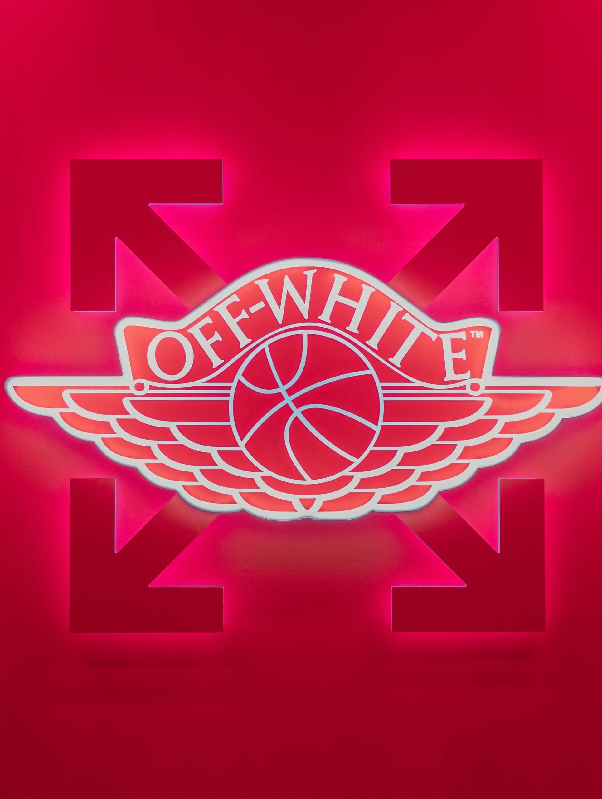 A red Off-White Air Jordan wings logo glowing on a red wall