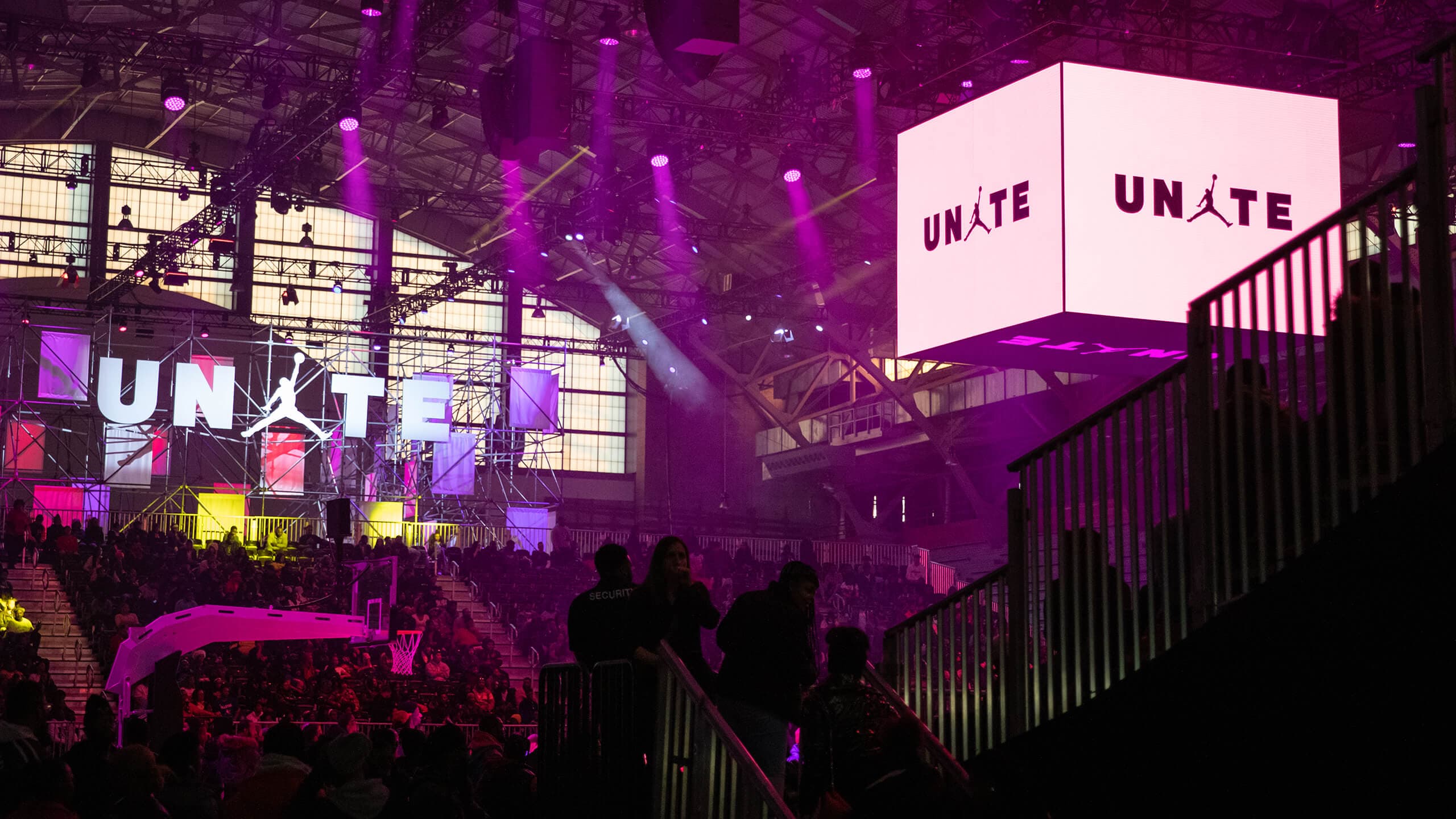 A crowd under purple light in front of the UNITE stage, with a glowing UNITE cube hanging above