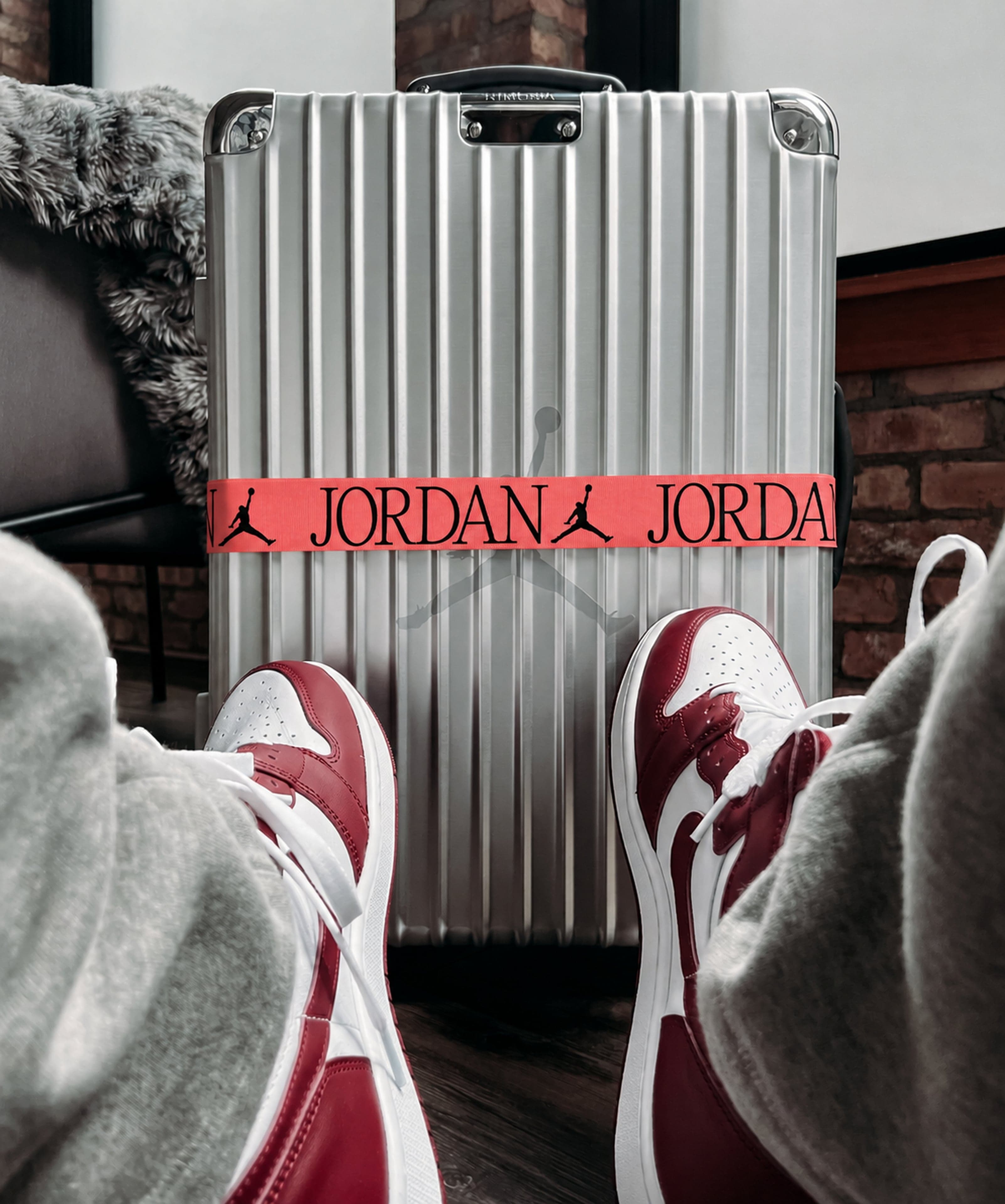 A silver suitcase with a red Jordan strap above feet in red and white sneakers