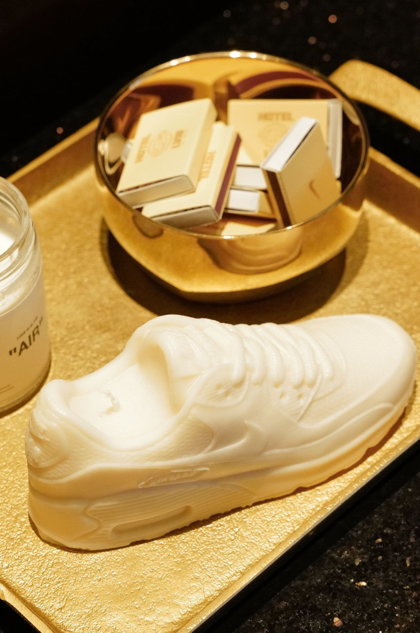 A gold tray holding a white sculpted Air Max shoe, a candle and gift boxes