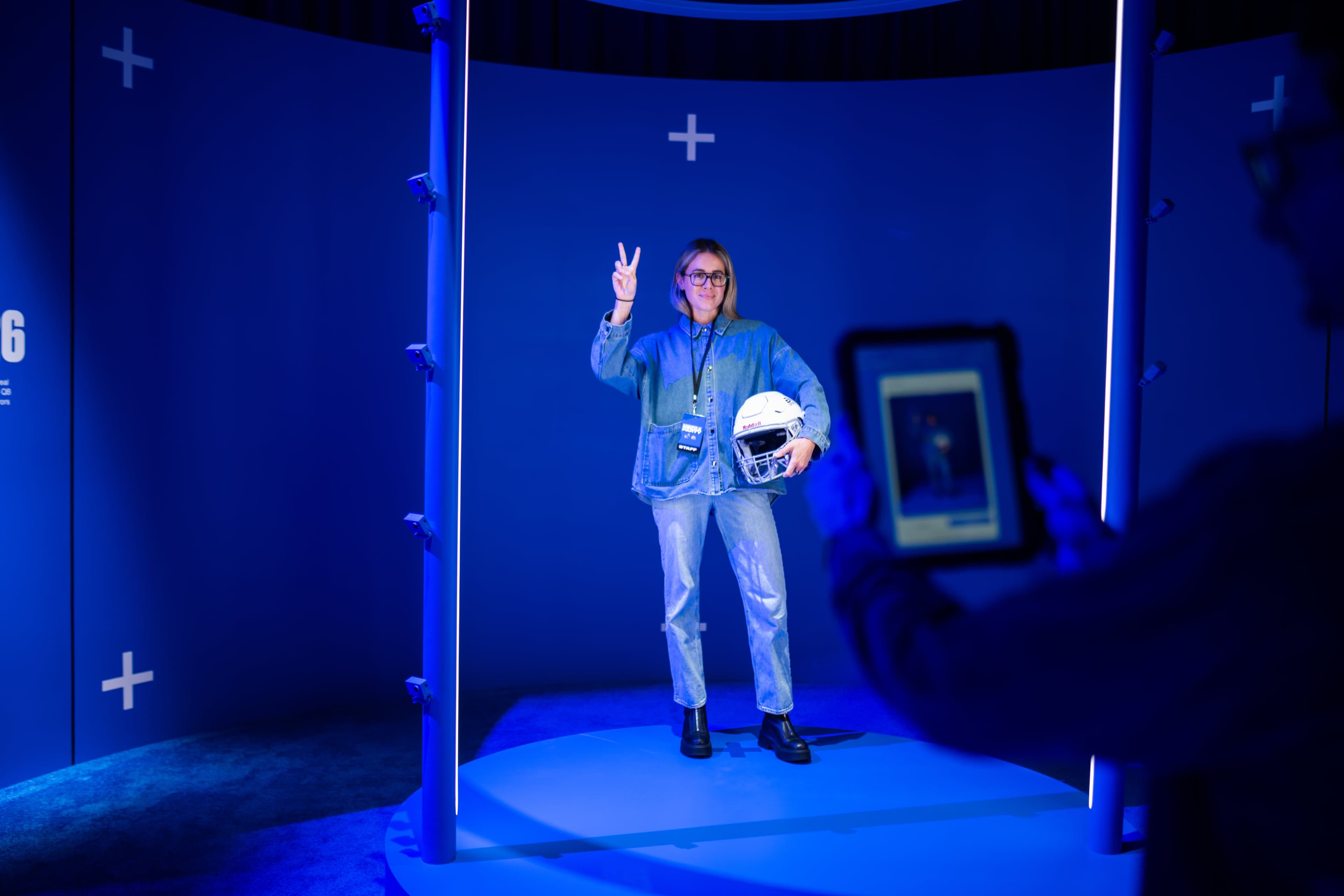 A guest posing with a football helmet inside the scanning rig while a staff member films them on a tablet