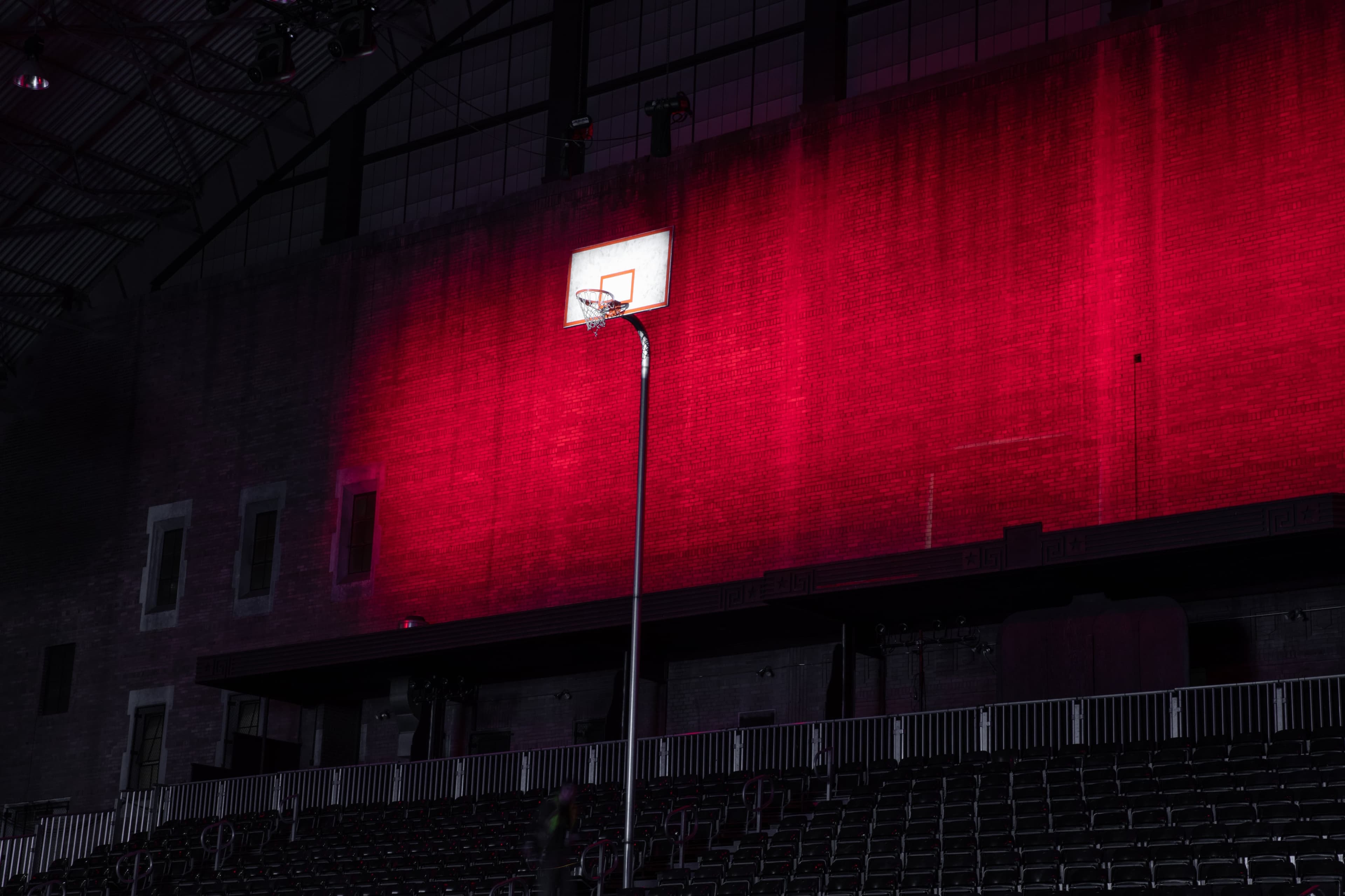 A basketball hoop in front of a red-lit wall in the dark arena