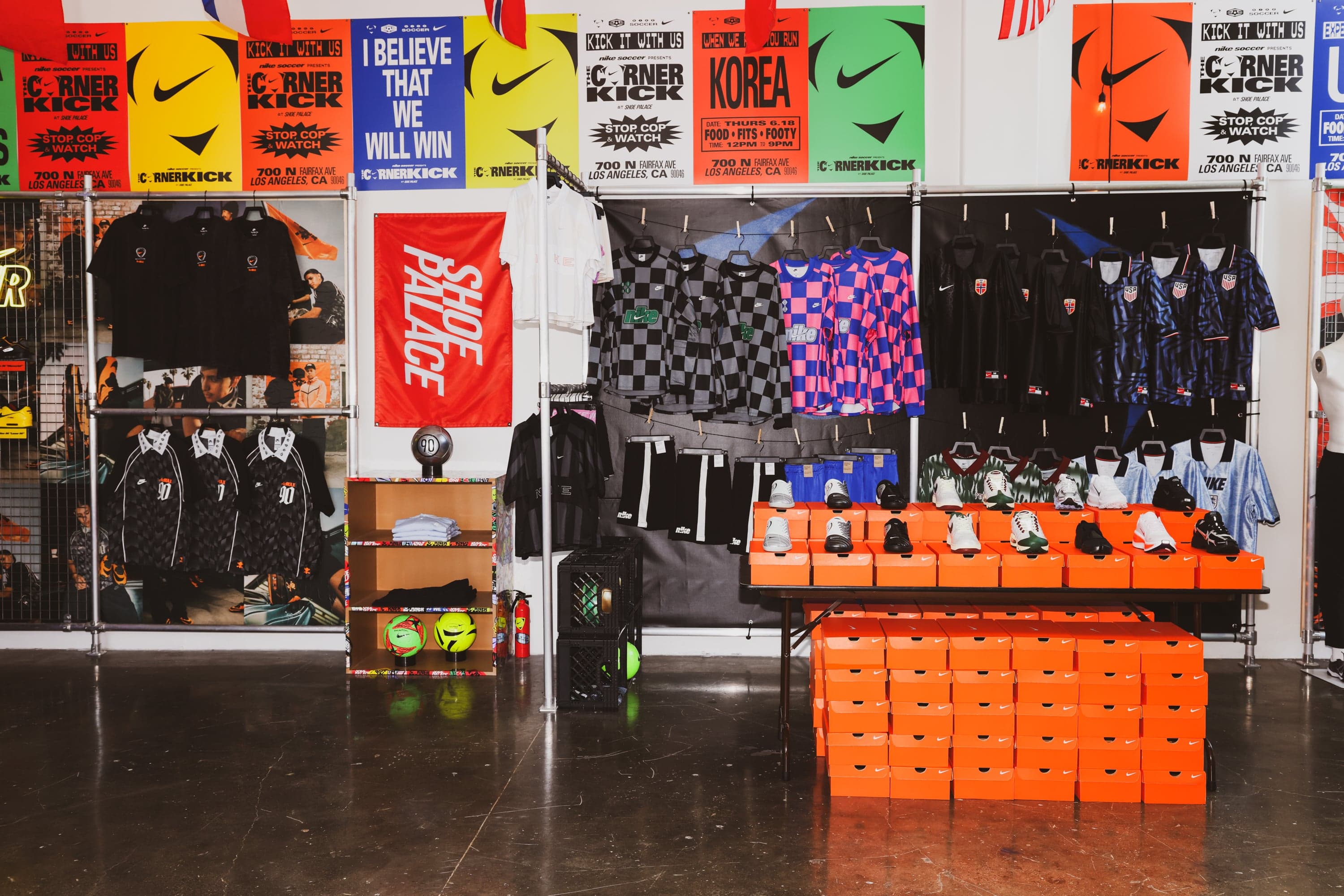 Retail wall with jerseys, sweatpants and a stack of orange shoe boxes under match posters