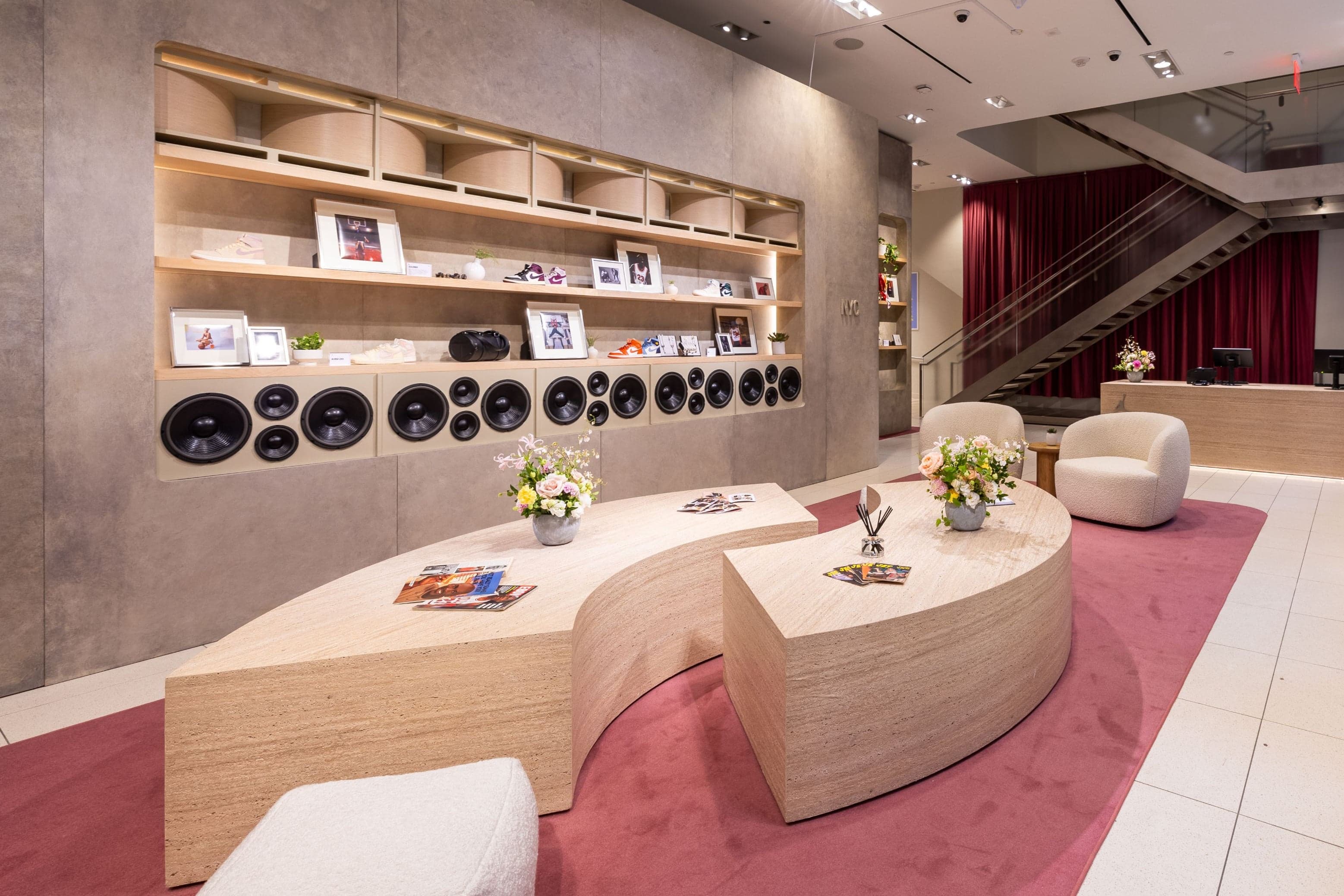 Curved wooden tables with flowers and magazines in front of a shelf wall of speakers and framed photos