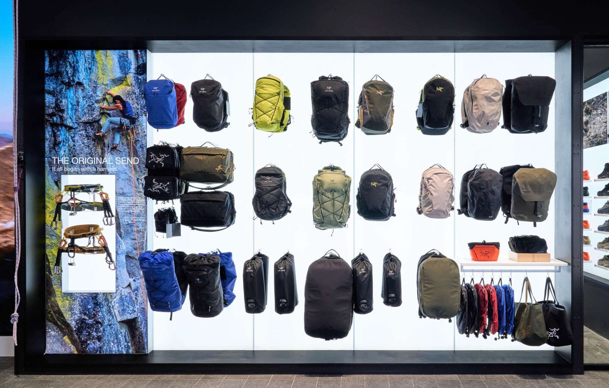 An illuminated wall of backpacks beside a climbing photograph