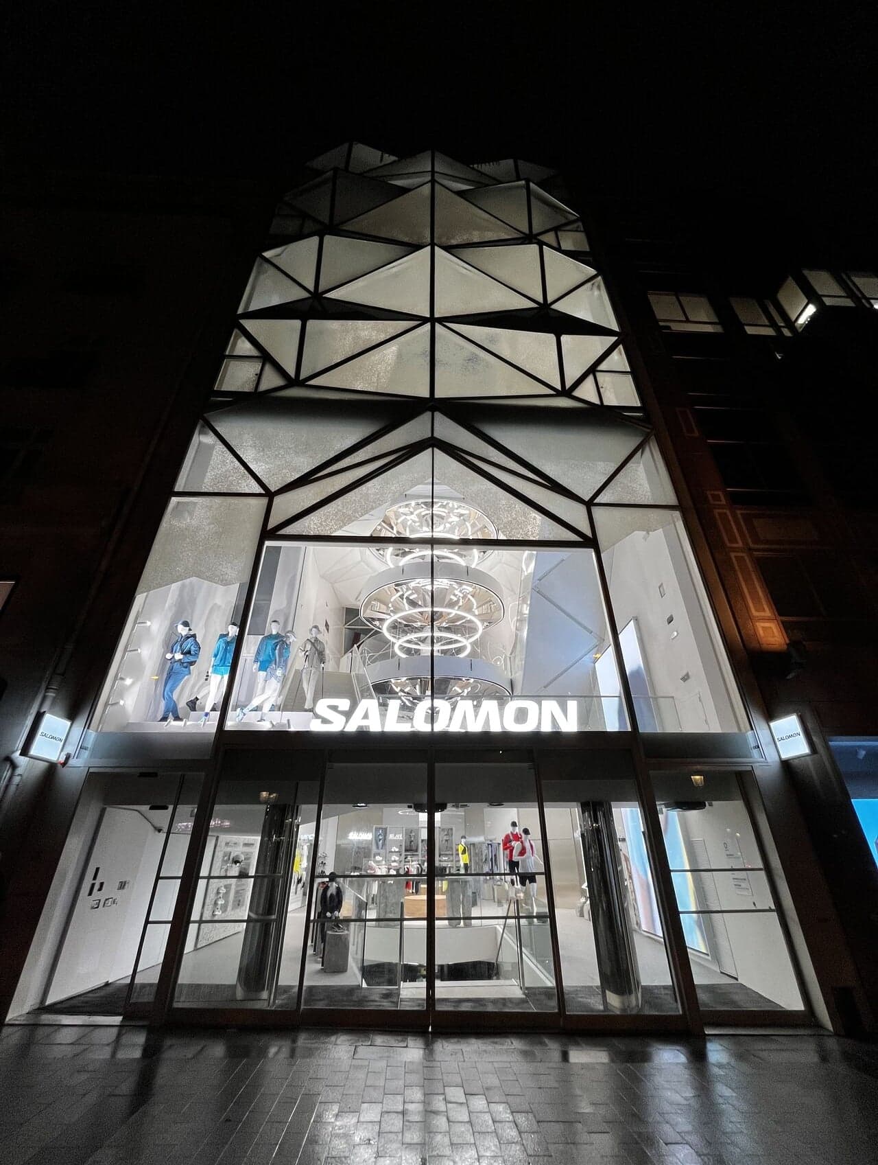 The Salomon store façade at night, its angular glass front lit from inside
