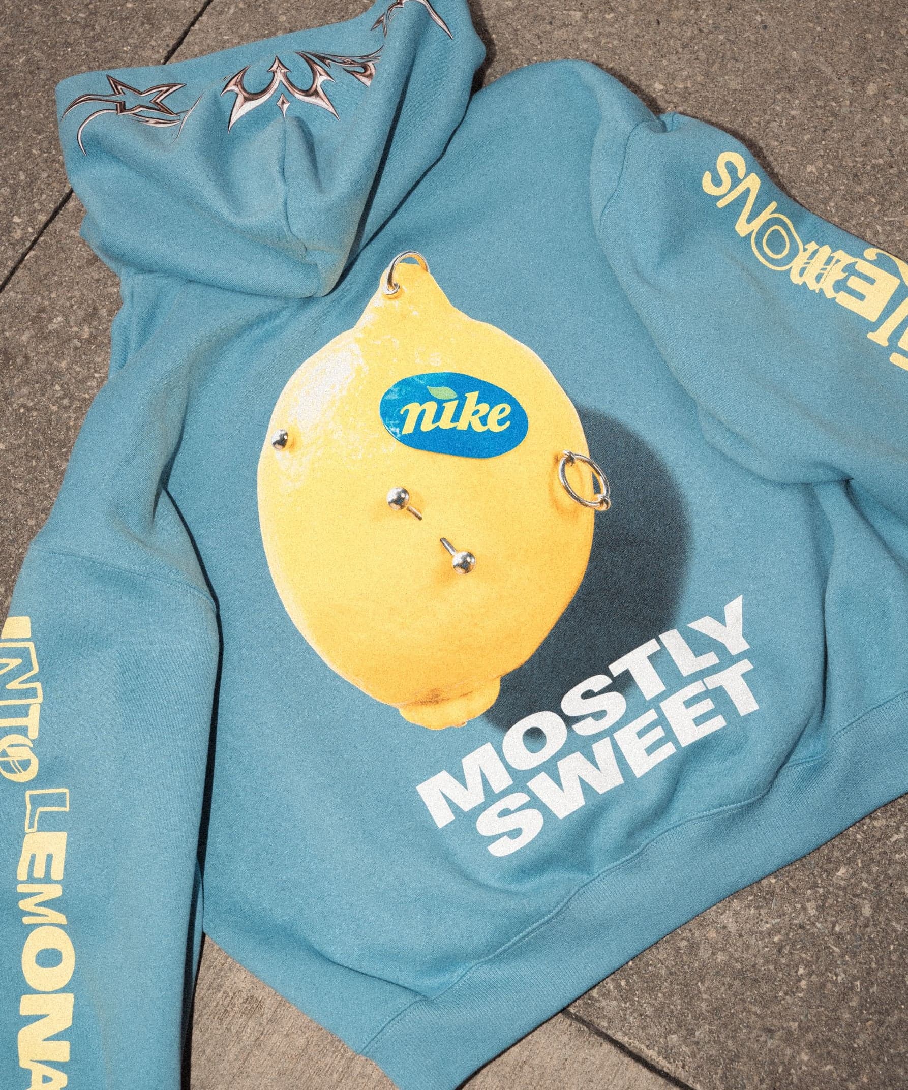 A blue hoodie printed with a lemon wearing a Nike sticker and the words “Mostly Sweet”