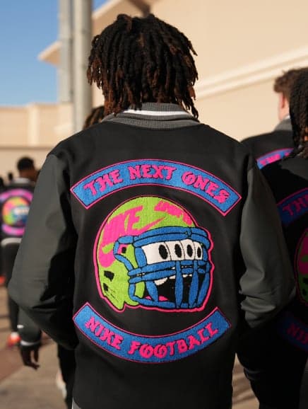 The back of a black varsity jacket embroidered “The Next Ones, Nike Football” around a helmet