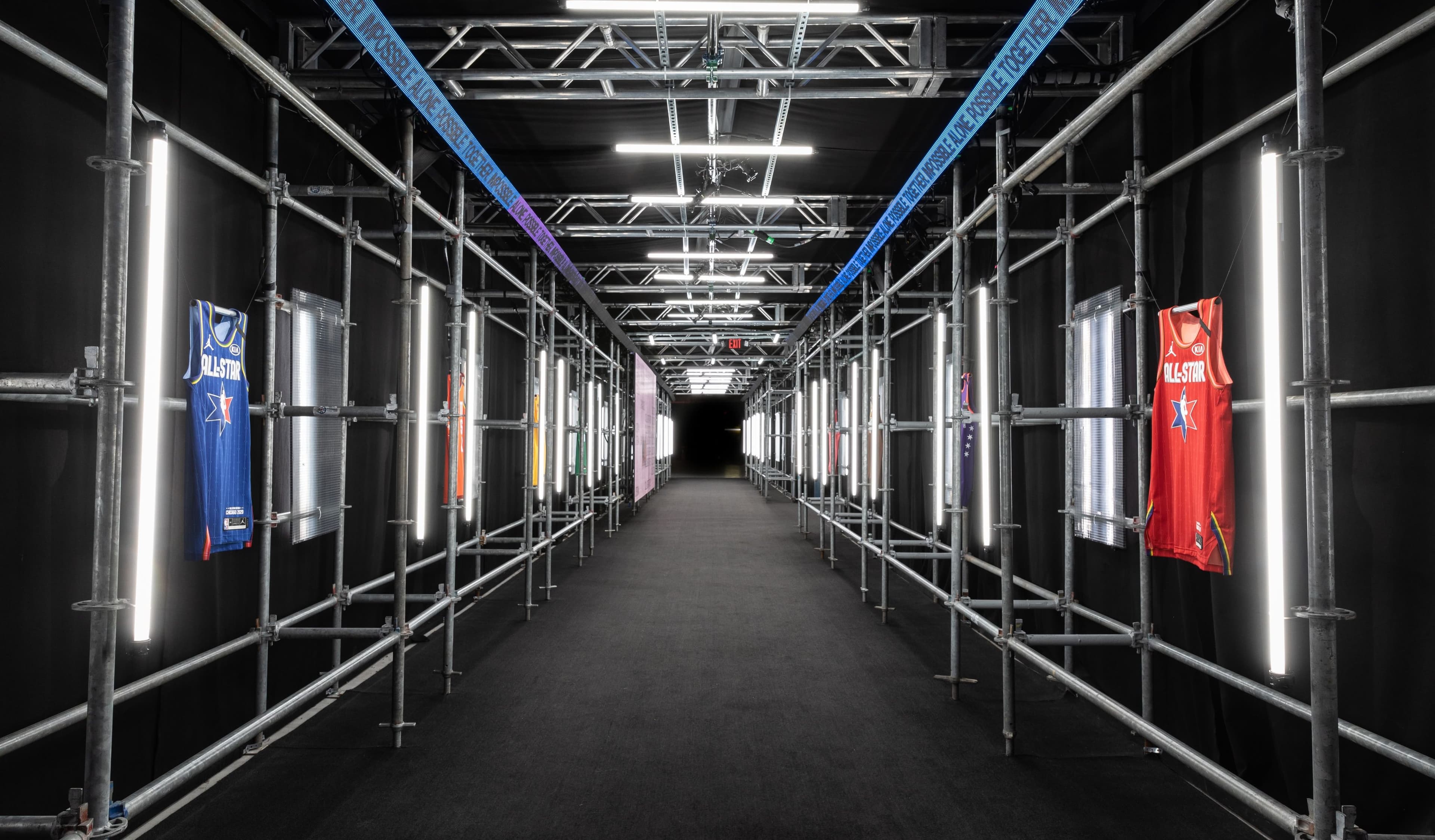 A long scaffolding tunnel lined with light tubes and hanging jerseys