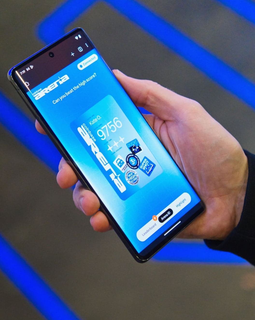 A hand holding a phone showing the Coinbase Arena microsite