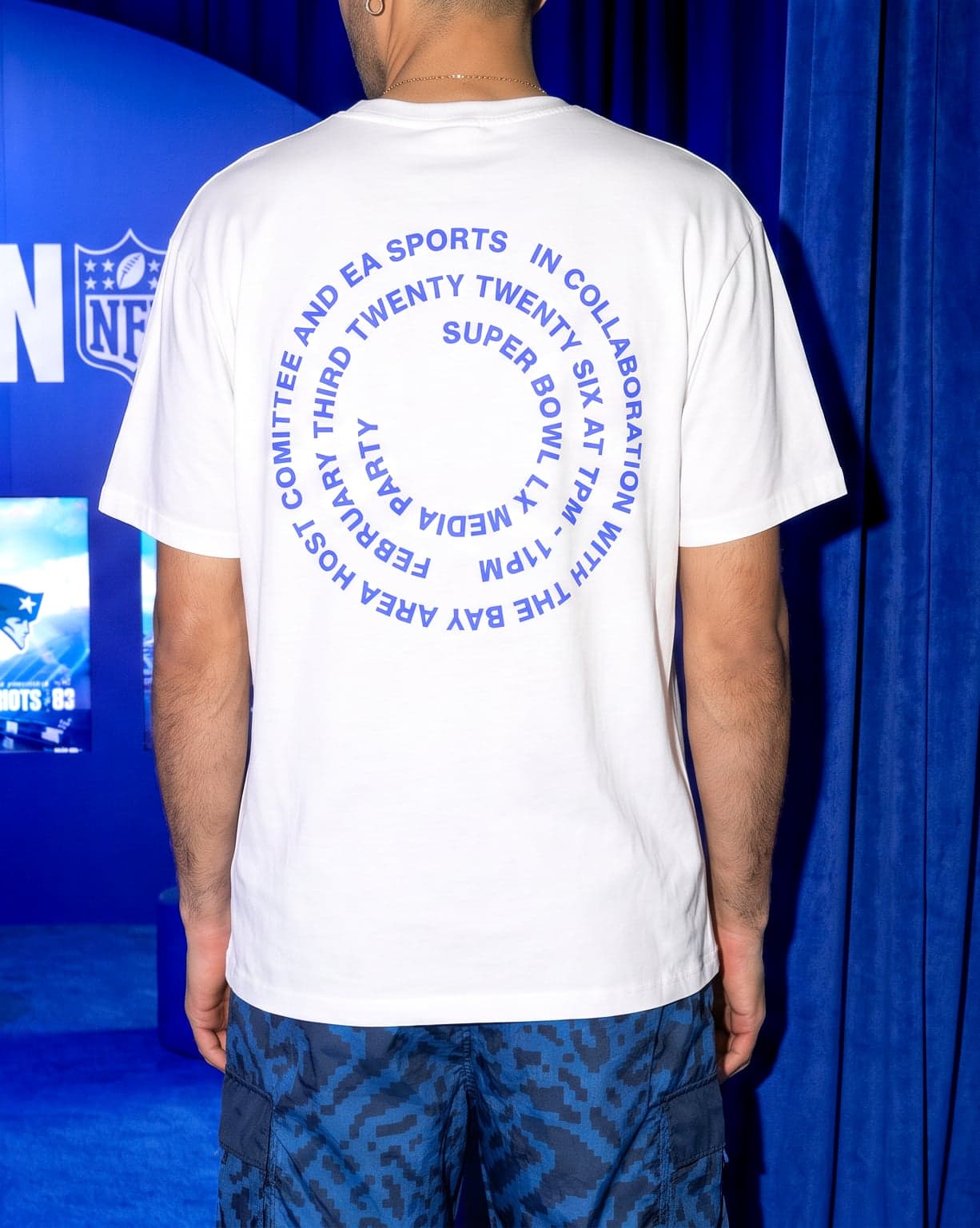 The back of the event t-shirt, printed with a circle of text about the Super Bowl media party, worn in front of the Madden lounge