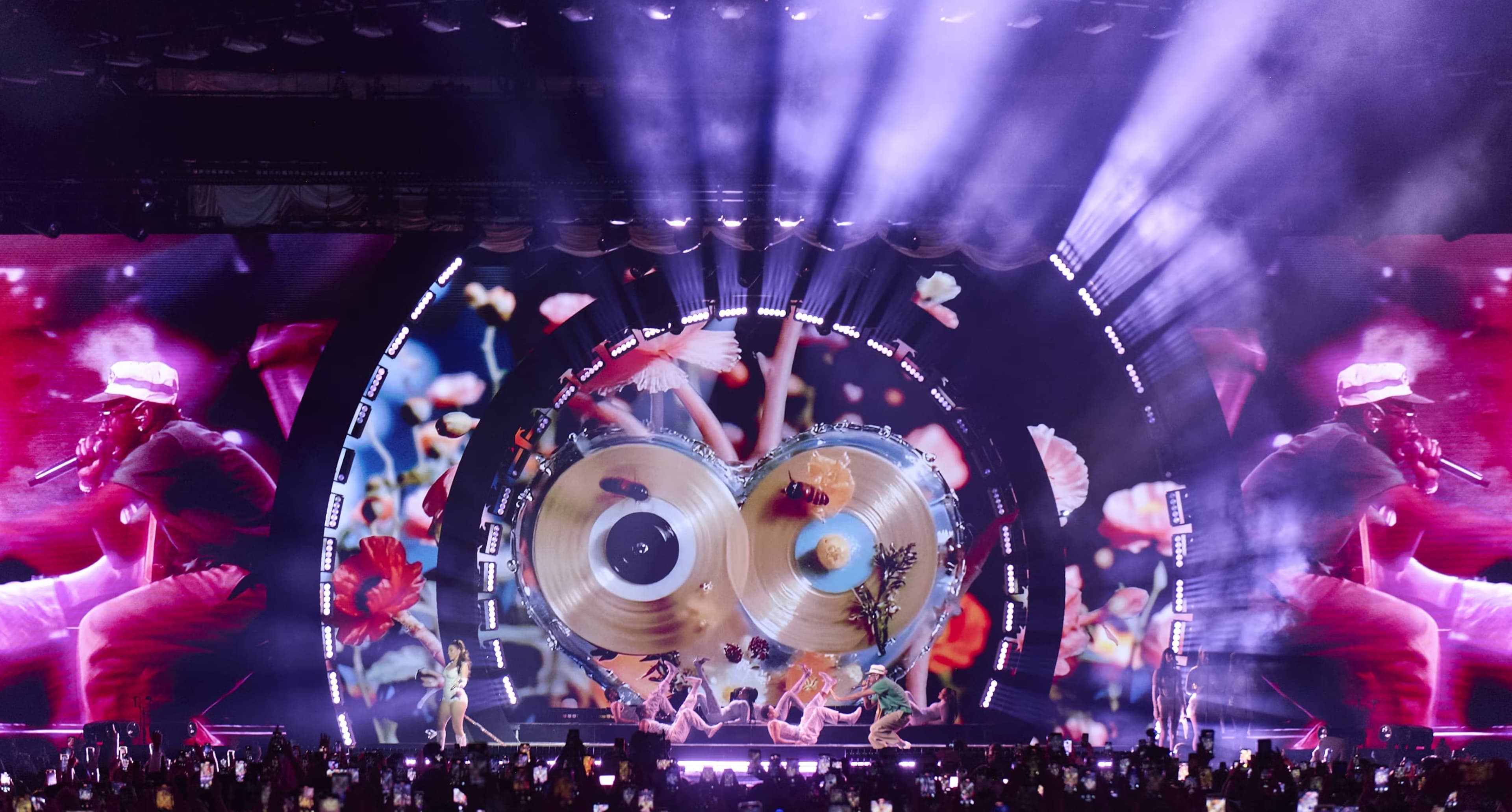 The stage lit purple with two gold discs on the curved LED wall and a crowd in front
