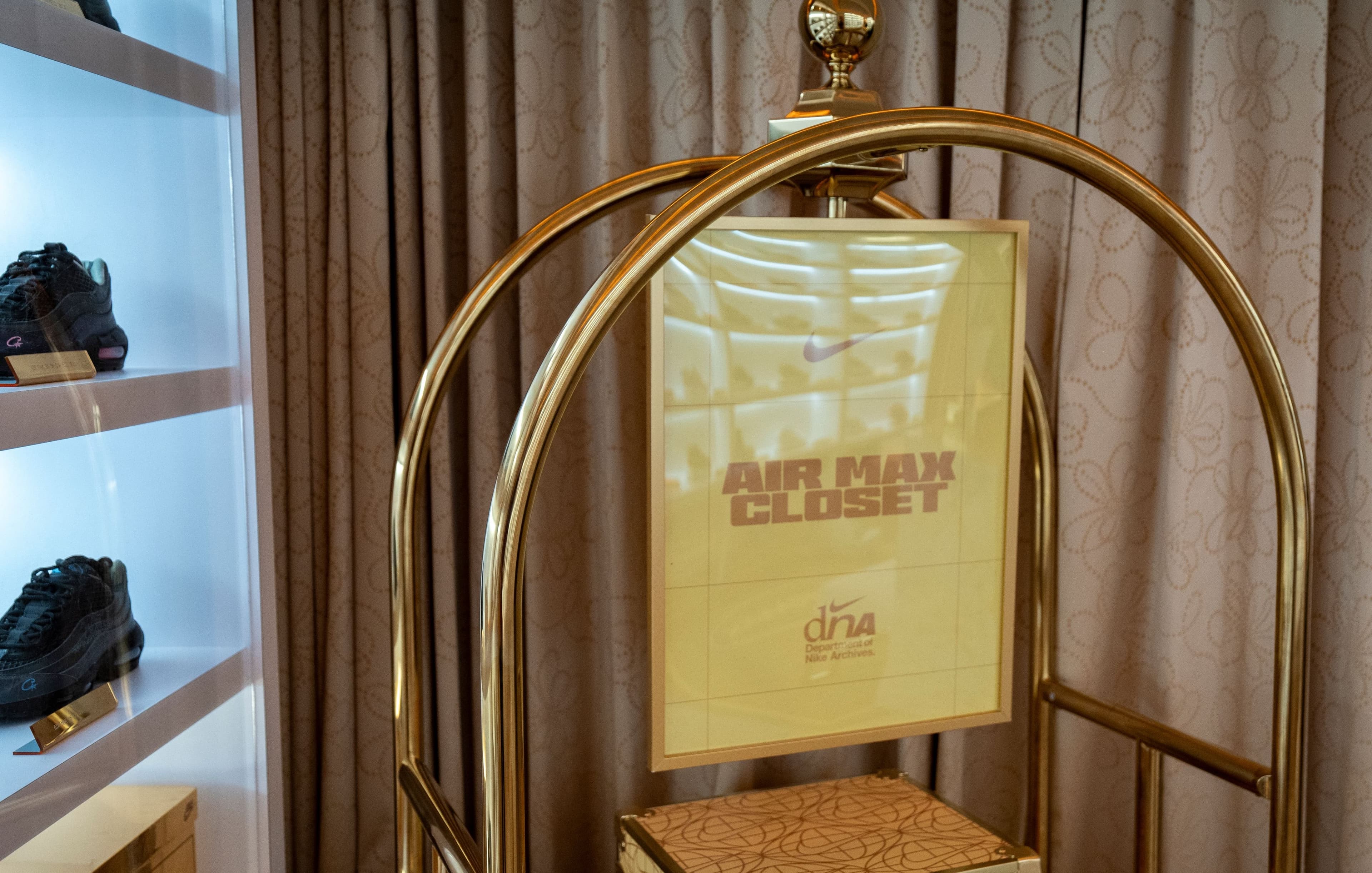 A gold bellhop cart holding an Air Max Closet sign, beside shelves of sneakers