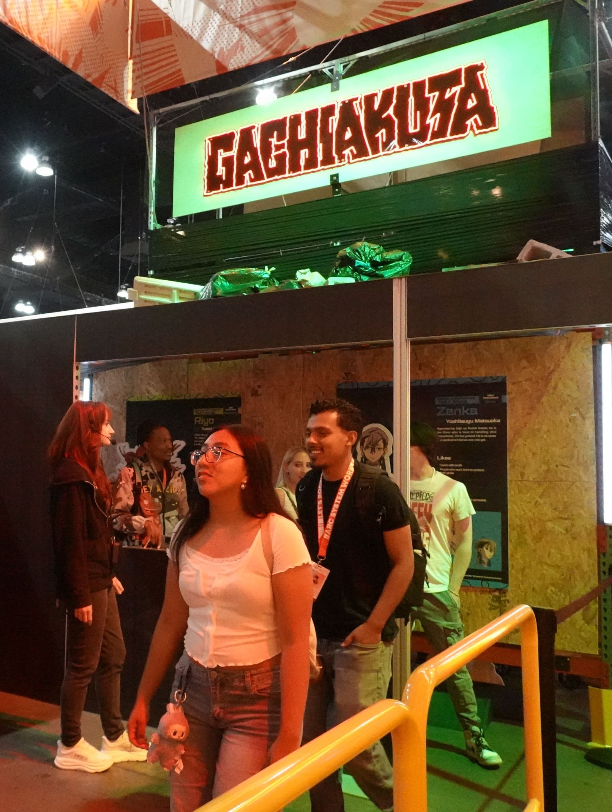 Fans looking up at the trash props beneath the lit Gachiakuta sign