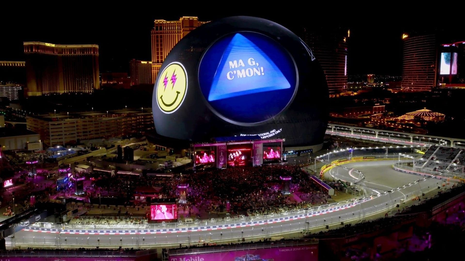 The Las Vegas Sphere lit as a giant Magic 8 Ball reading “Ma G, C’mon!” beside the Grand Prix track at night
