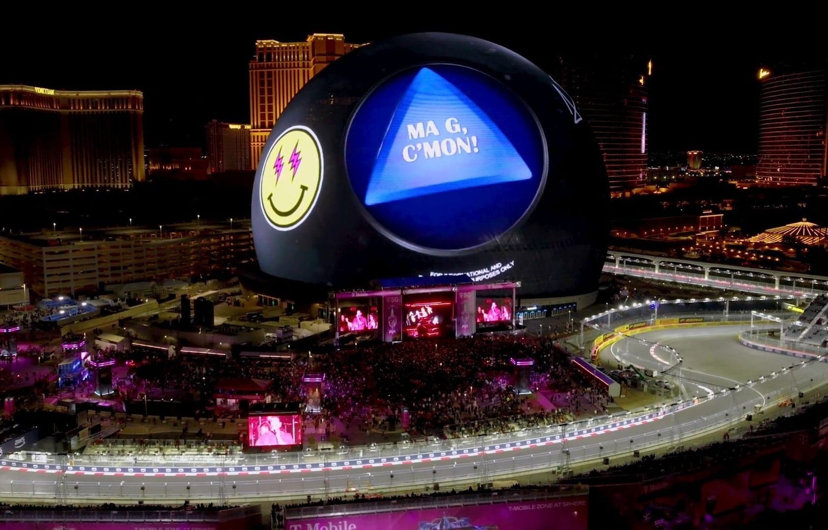 The Las Vegas Sphere lit as a giant Magic 8 Ball reading “Ma G, C’mon!” beside the Grand Prix track at night
