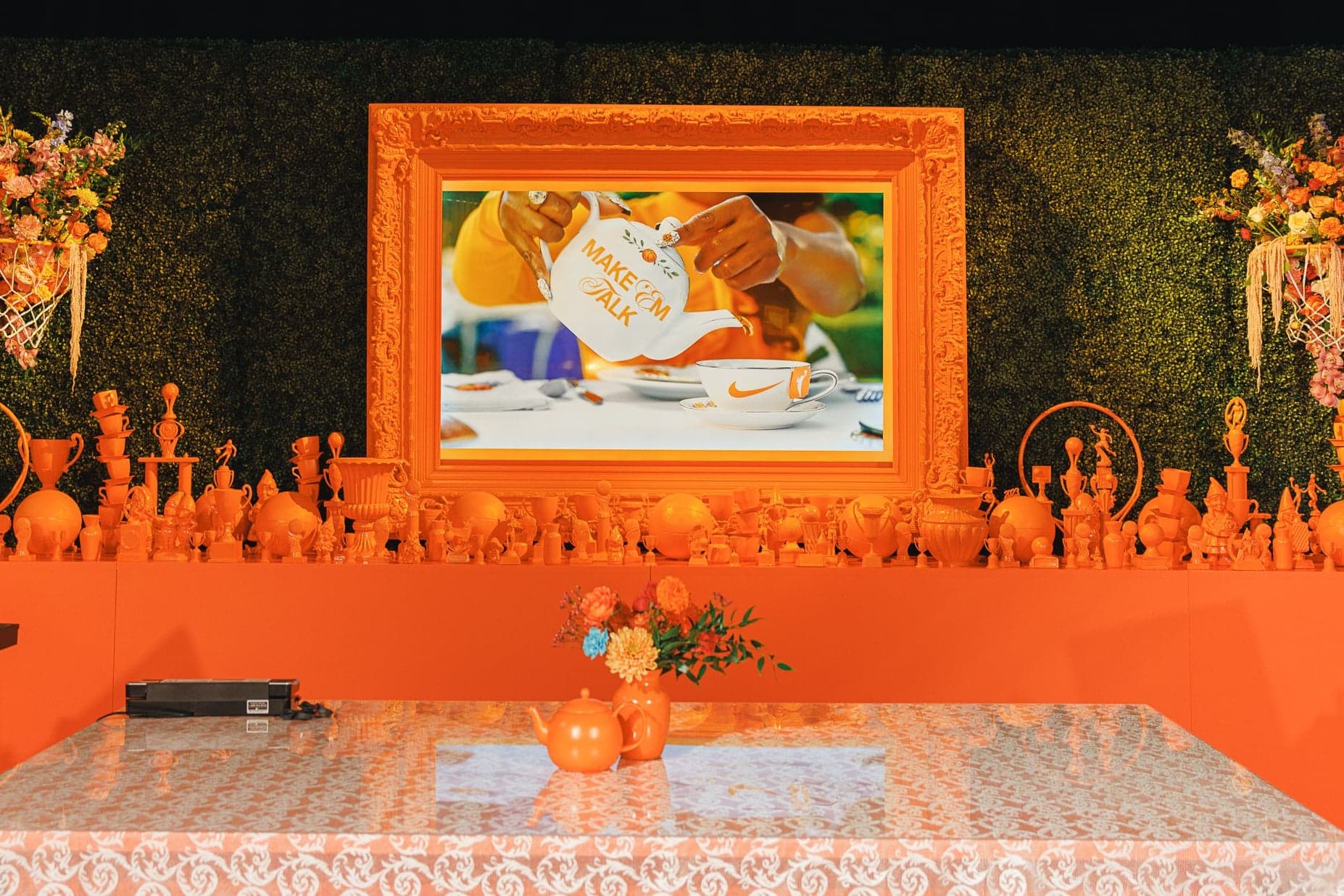 A gold-framed painting above a shelf of orange figurines and flowers